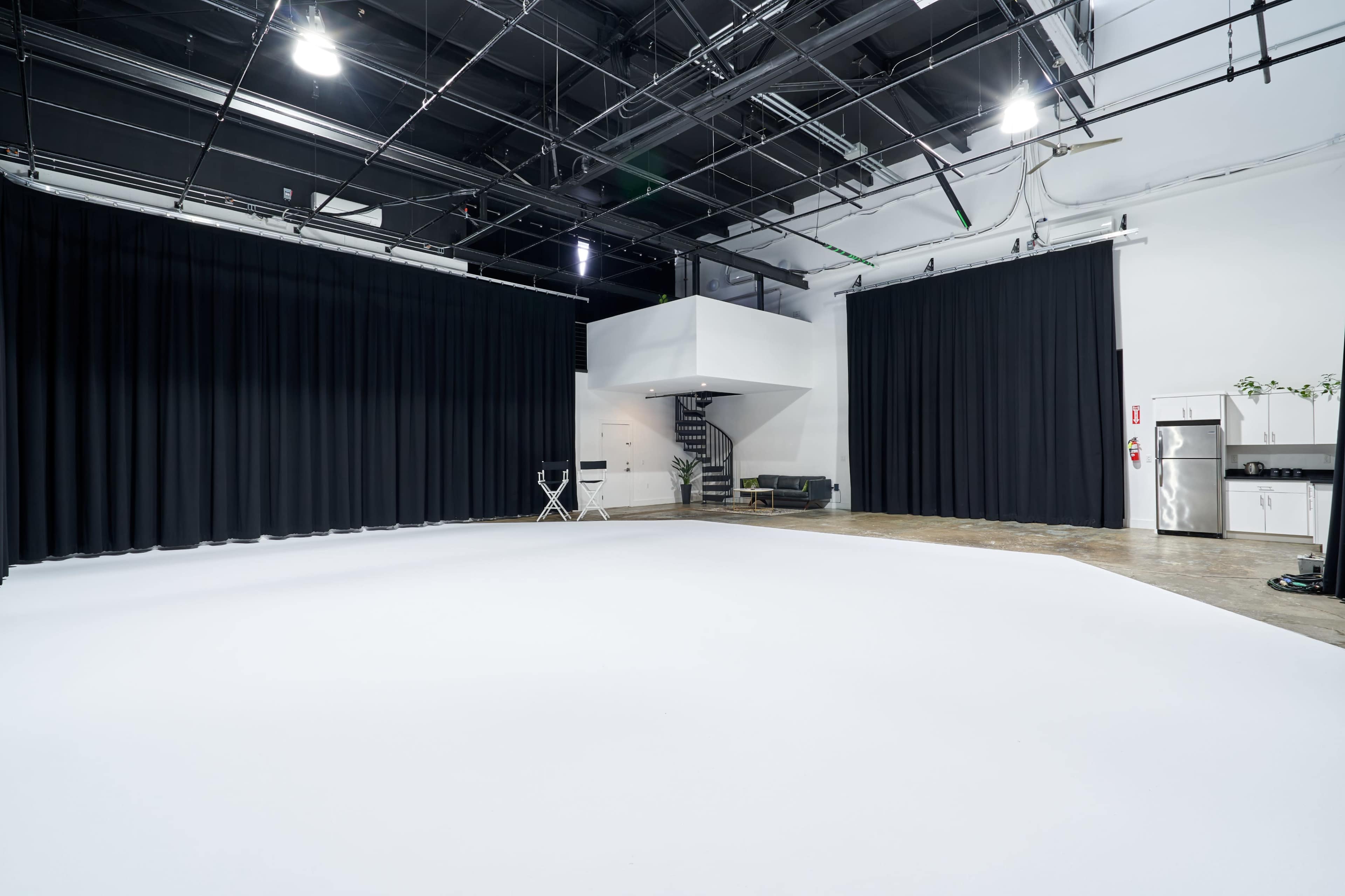 A large, empty studio space with black curtains, white flooring, and modern furnishings.