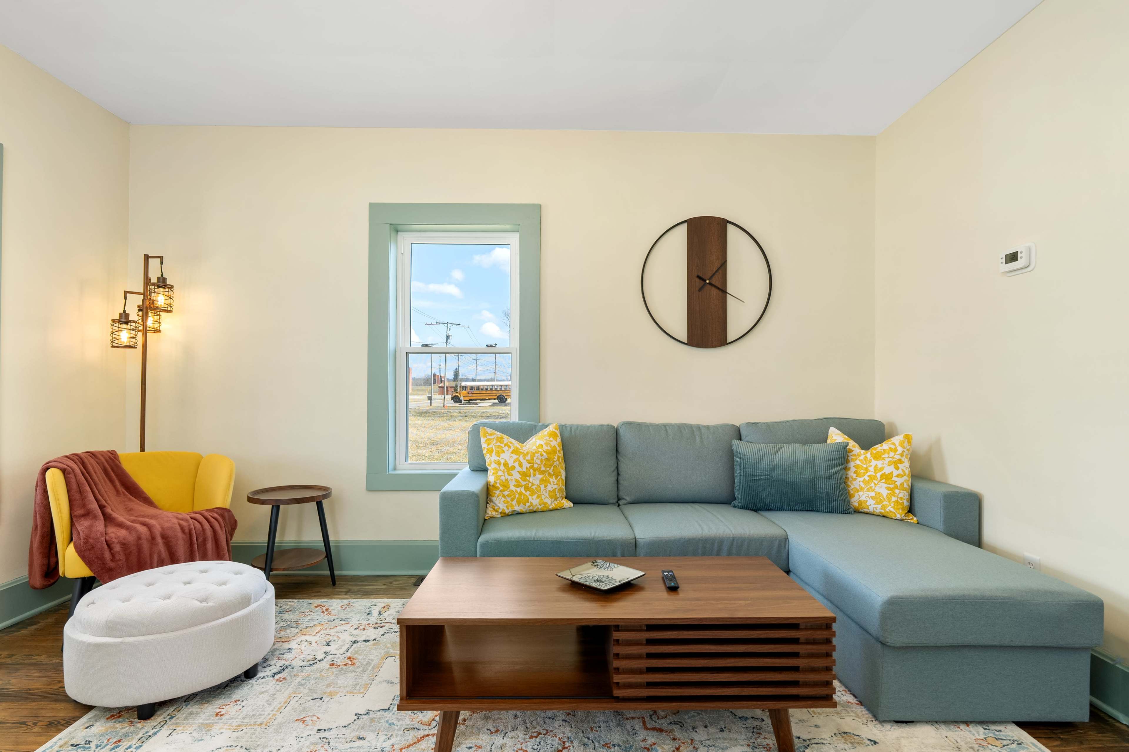 The living room features a blue sectional sofa with yellow accent pillows, a wooden coffee table, and a cozy armchair beside a window.