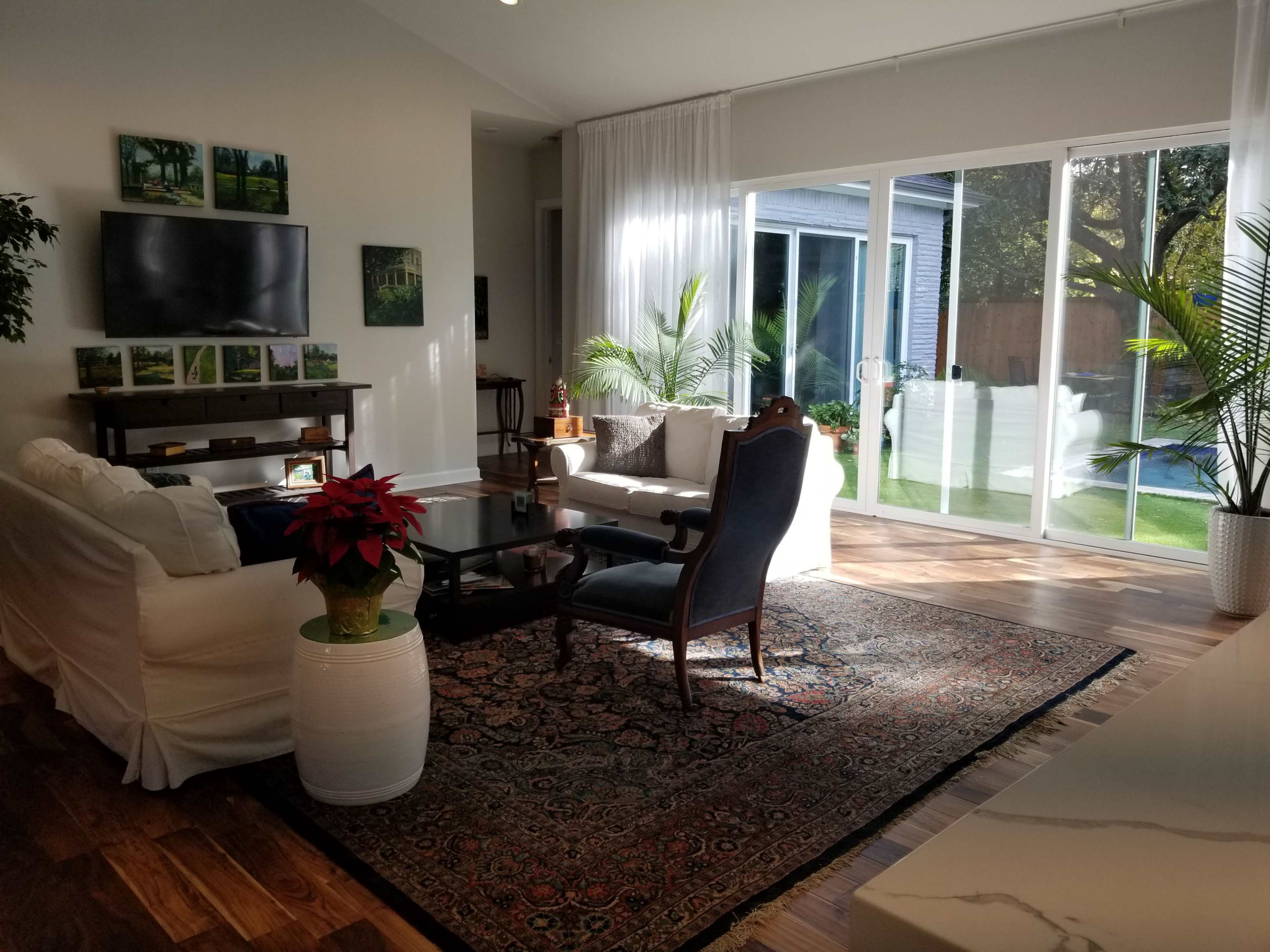 The living room features a white sofa, a dark wooden chair, and a large rug, with sliding glass doors leading to a grassy outdoor area.