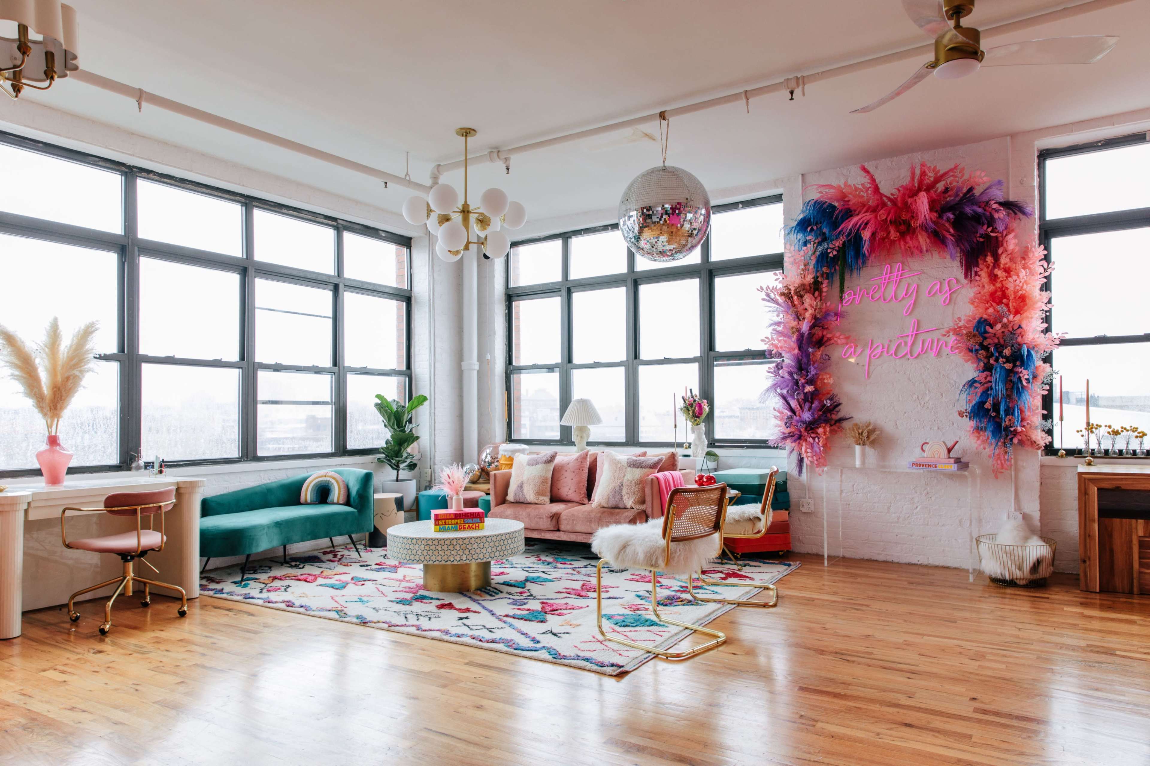 A brightly decorated living room features large windows, colorful furniture, and a wall adorned with vibrant decorations.
