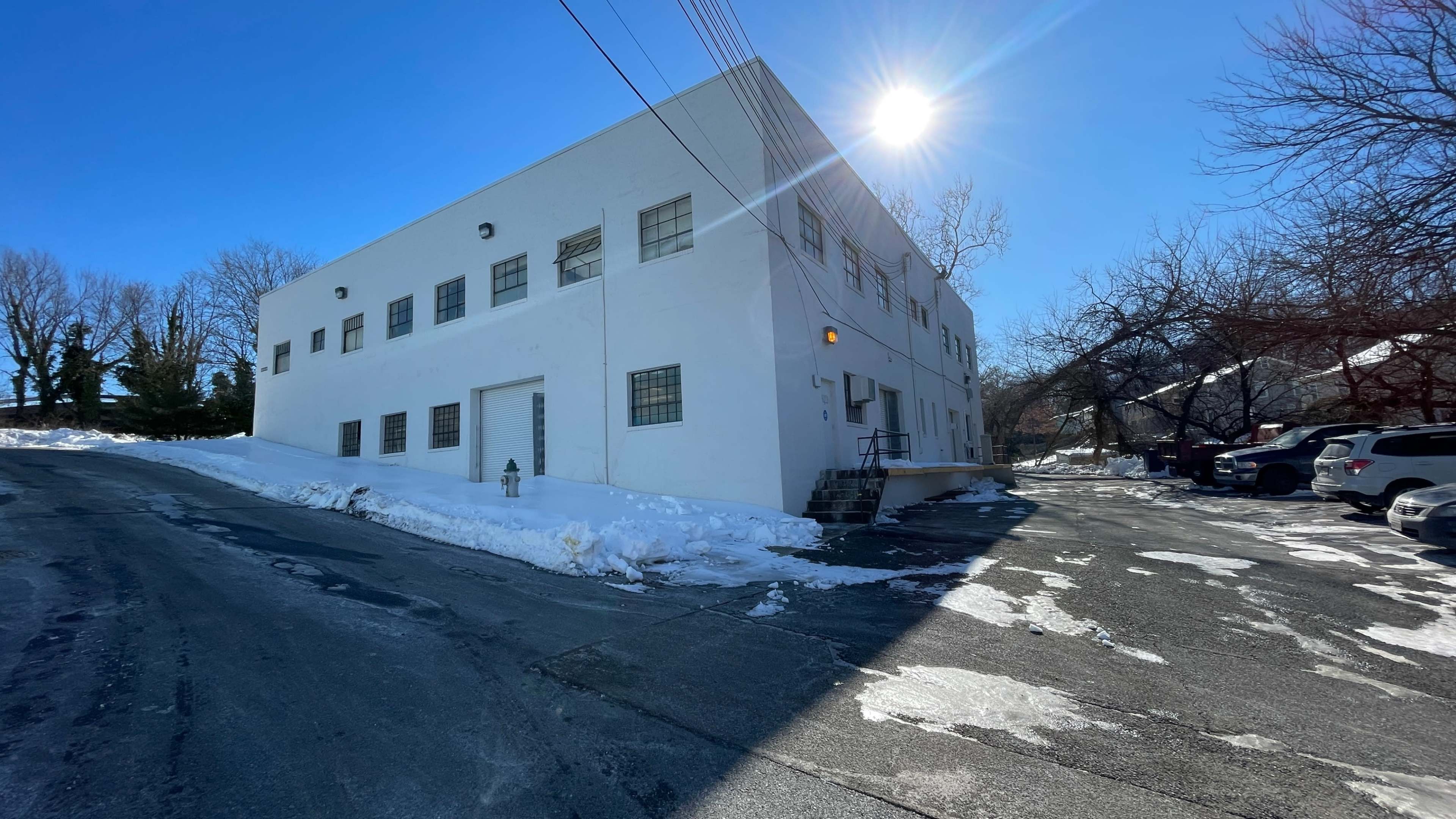 A white building stands at the end of a snow-covered driveway under a clear blue sky, with the sun shining brightly.