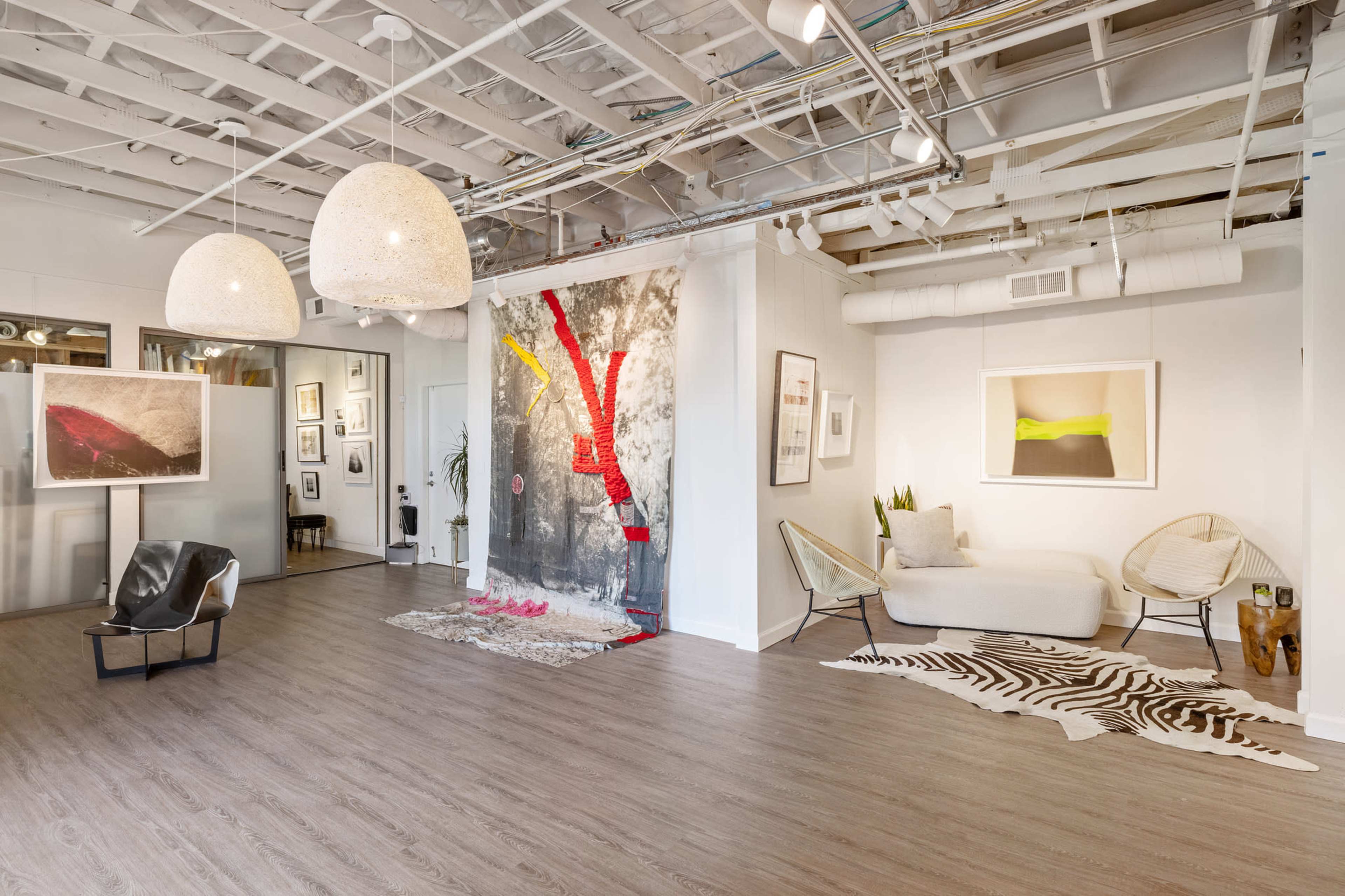 A modern art gallery interior with three large pendant lights, a seating area, and a vibrant abstract artwork displayed on the wall.