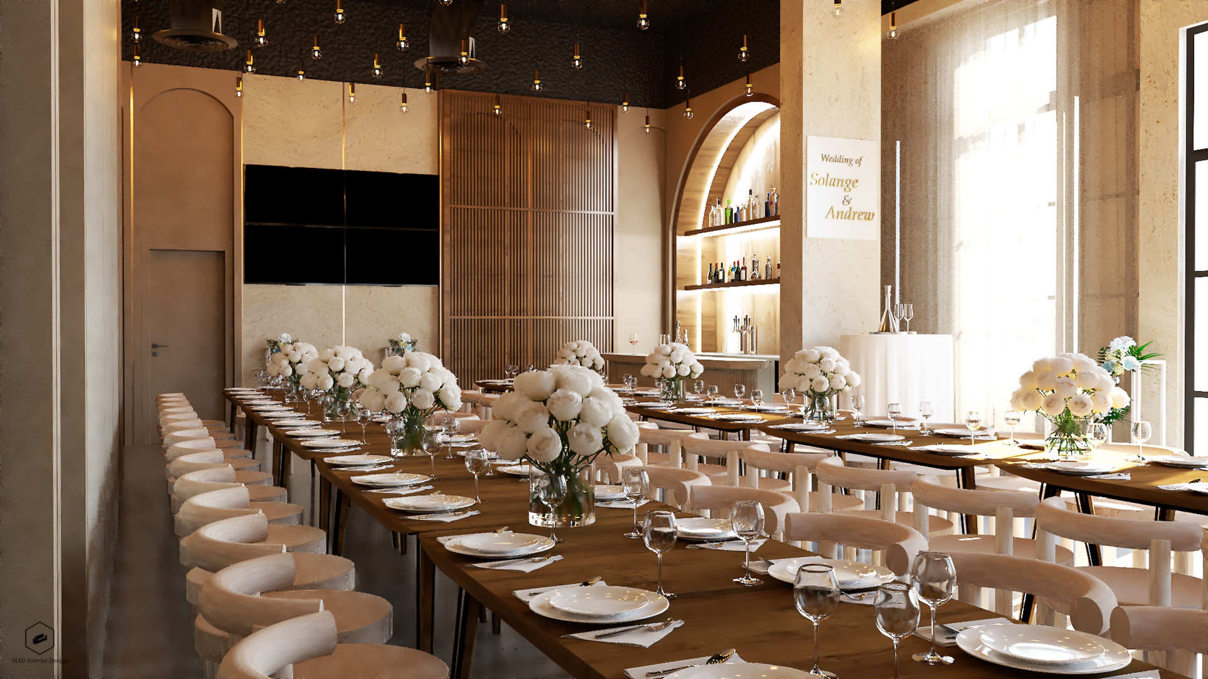 A long wooden dining table is set with plates, glasses, and floral centerpieces in a well-lit, elegantly decorated restaurant interior.