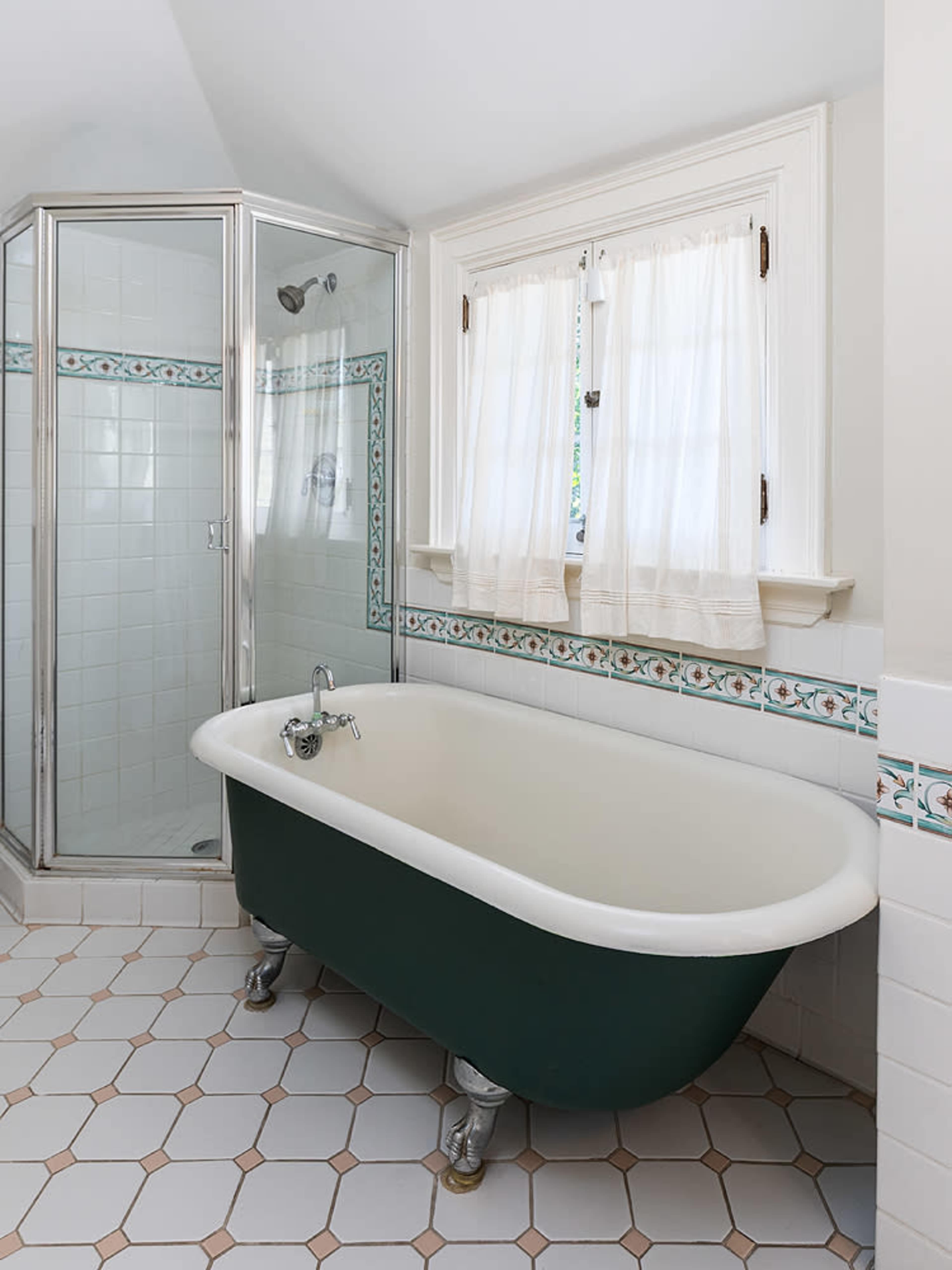 The image shows a bathroom featuring a clawfoot bathtub, a glass shower enclosure, and white tile flooring with decorative trim.