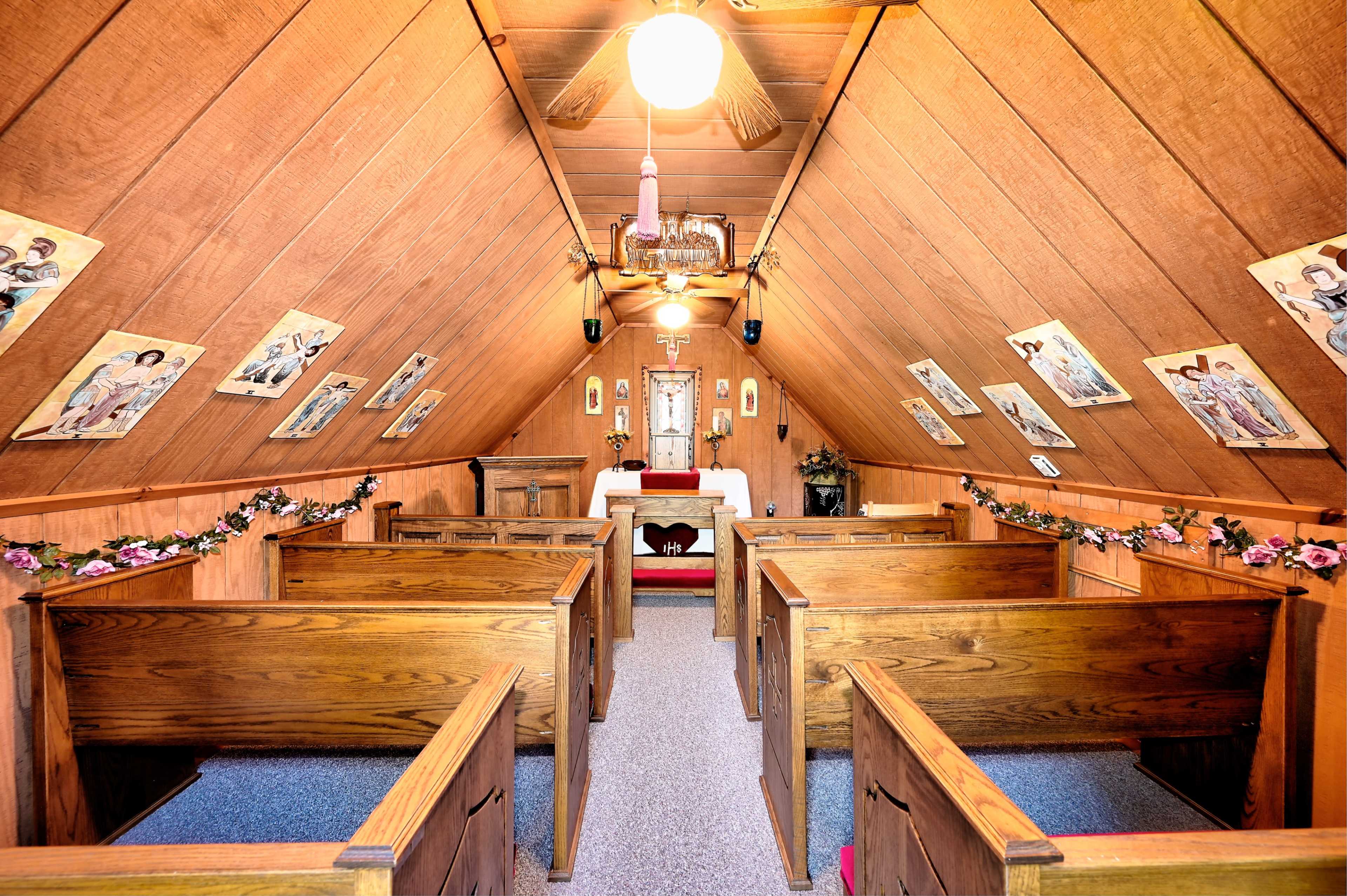 The interior of a wooden chapel with pews arranged facing an altar, adorned with religious icons on the walls.