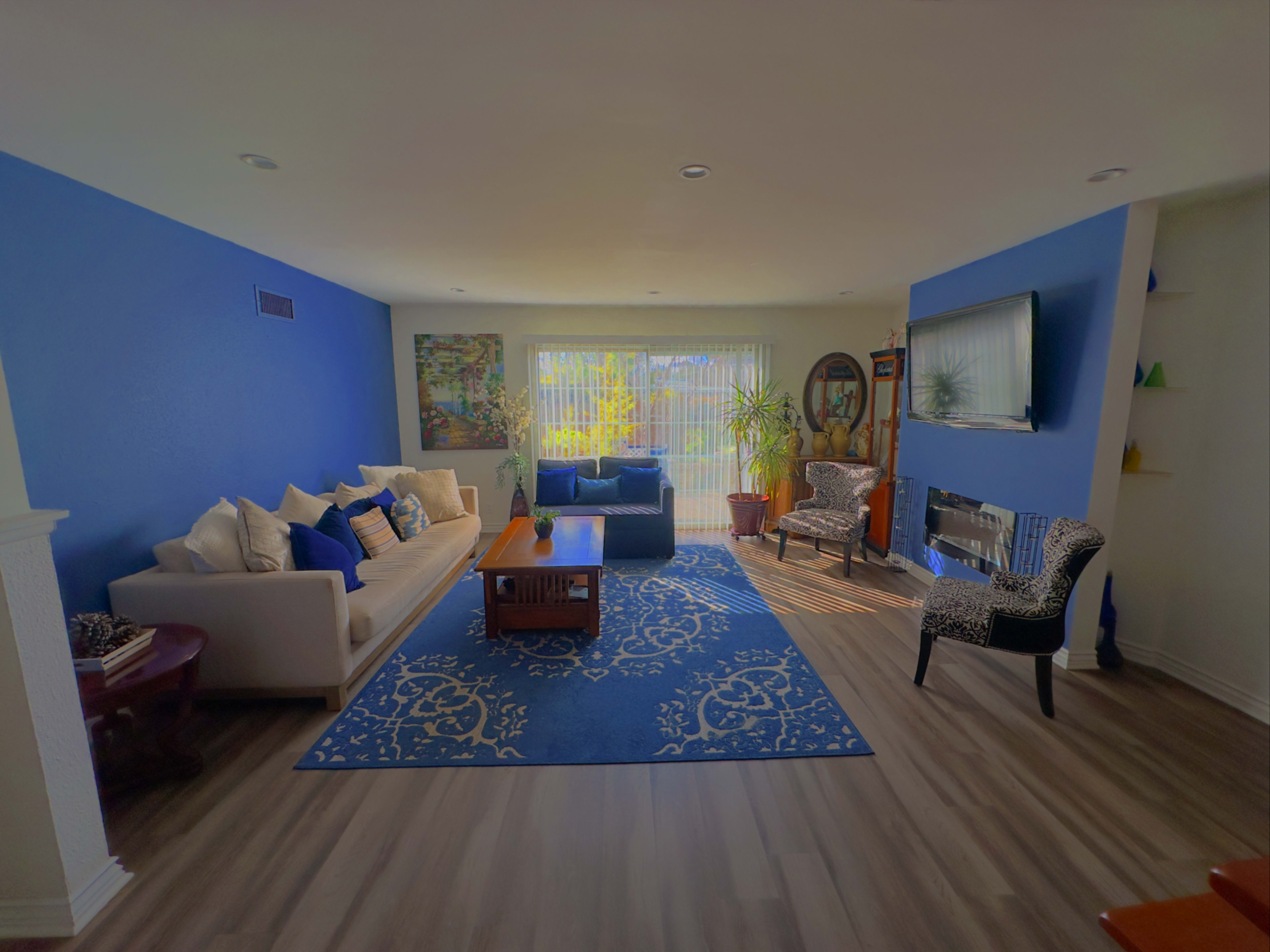 A living room with blue accent walls, a light-colored sofa, a patterned armchair, a coffee table, and a large window with natural light filtering in.