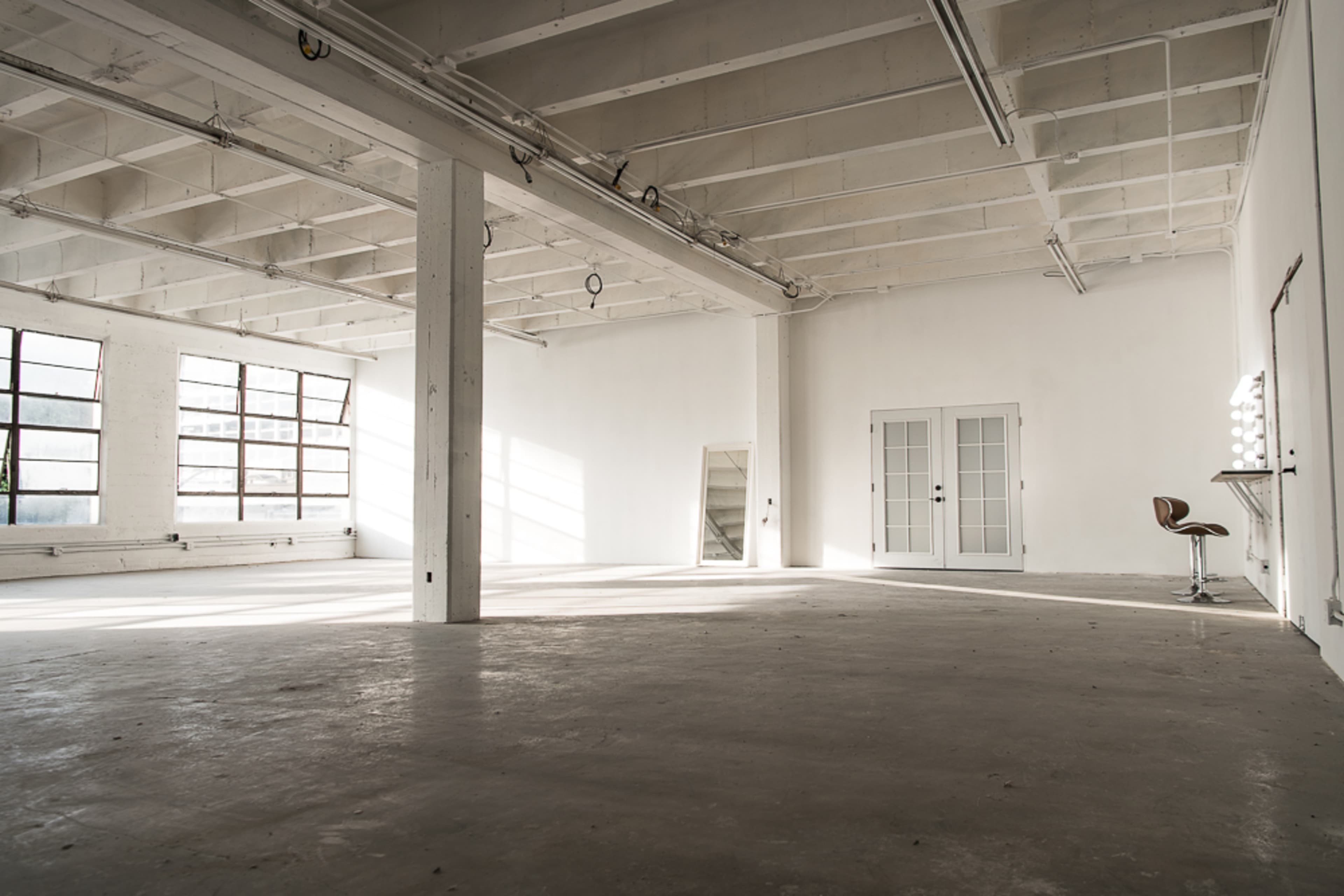 A spacious, empty room with large windows, concrete flooring, and minimal furnishings.