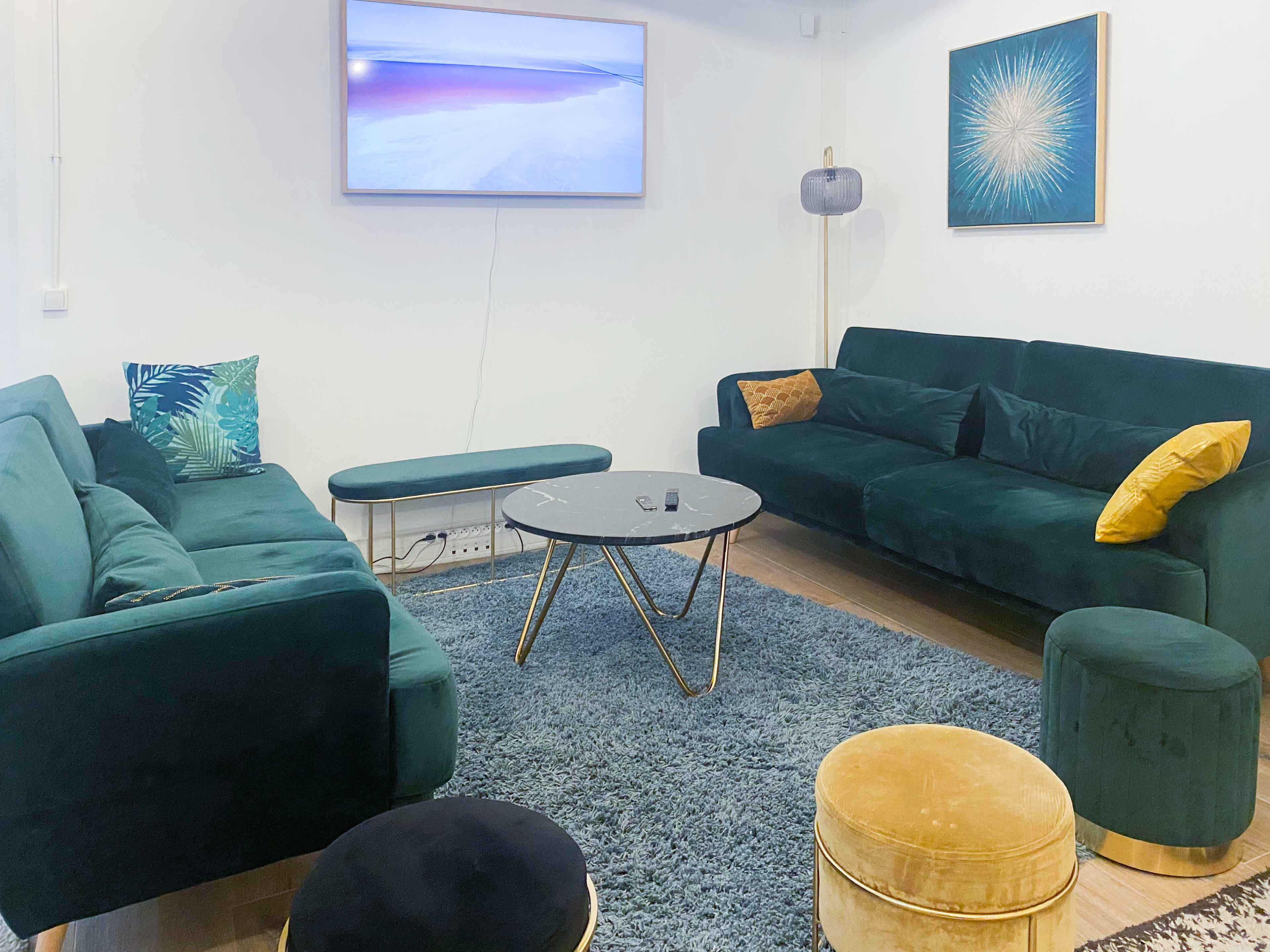 A modern living room with two green sofas, a gold and glass coffee table, and a large wall-mounted TV, all situated on a plush gray rug.