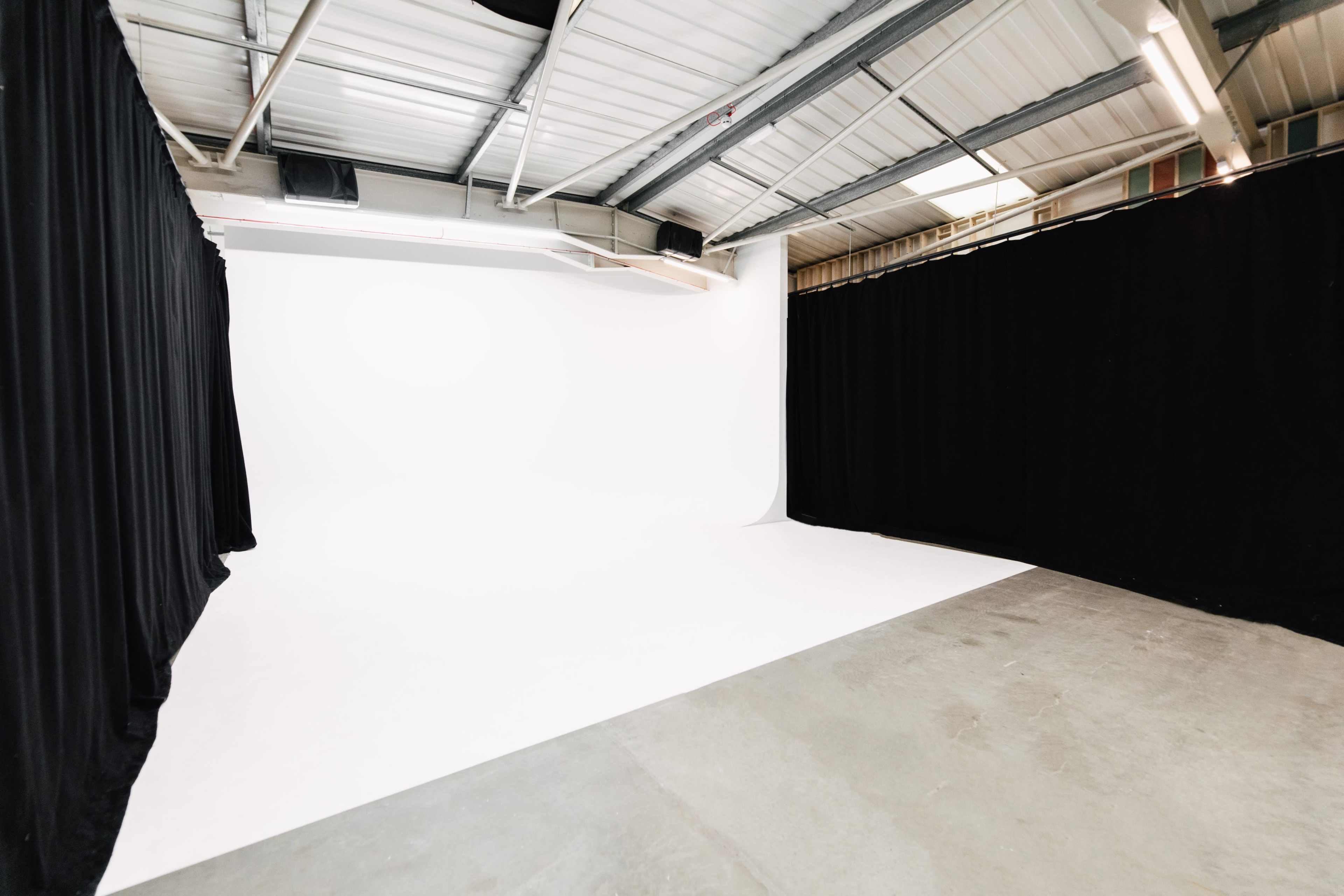 The image shows a photography studio with a white backdrop and black curtains on the sides.
