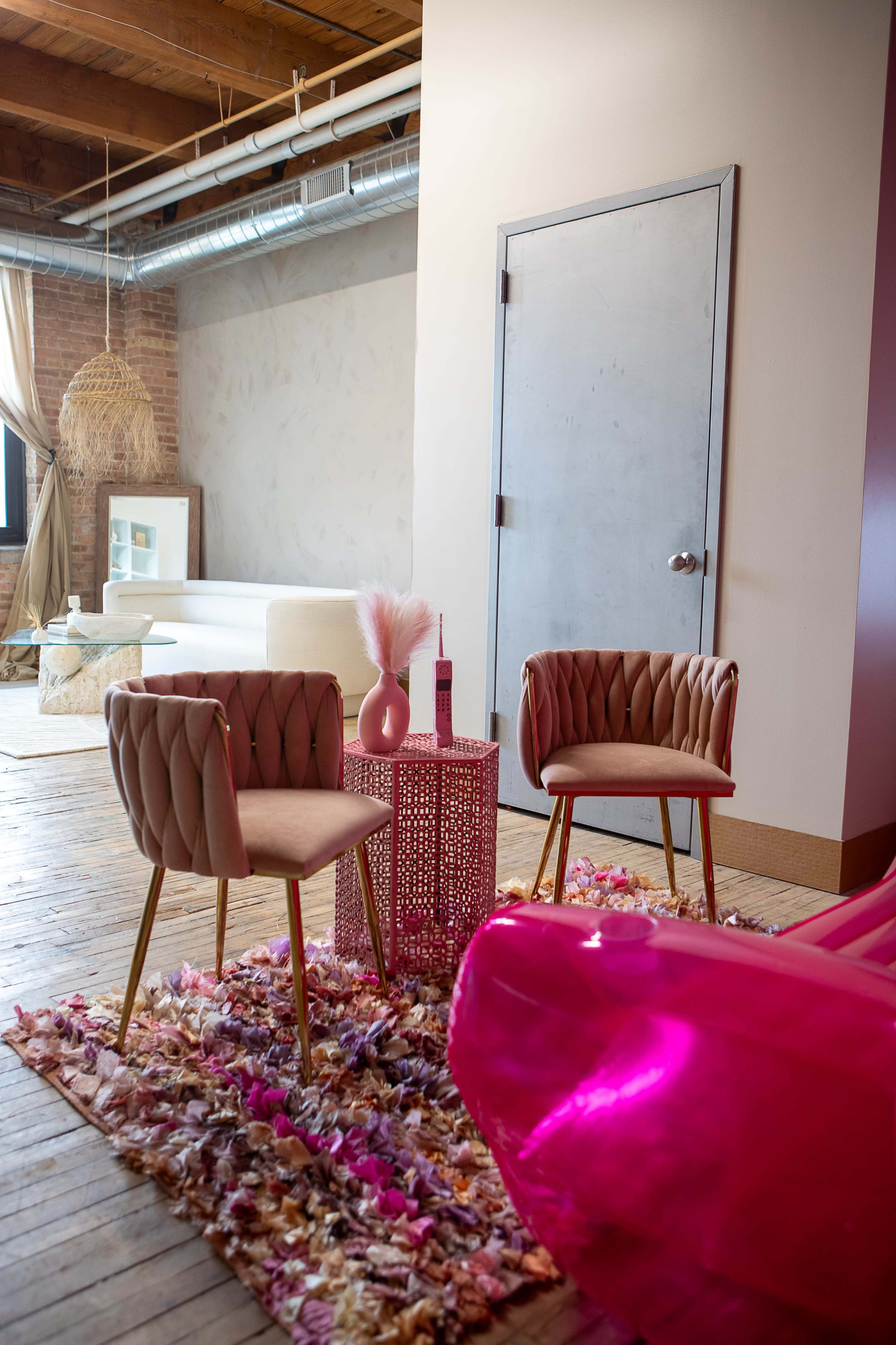 A cozy interior featuring two tufted chairs, a decorative table, and a rug made of colorful petals in a brightly lit room.