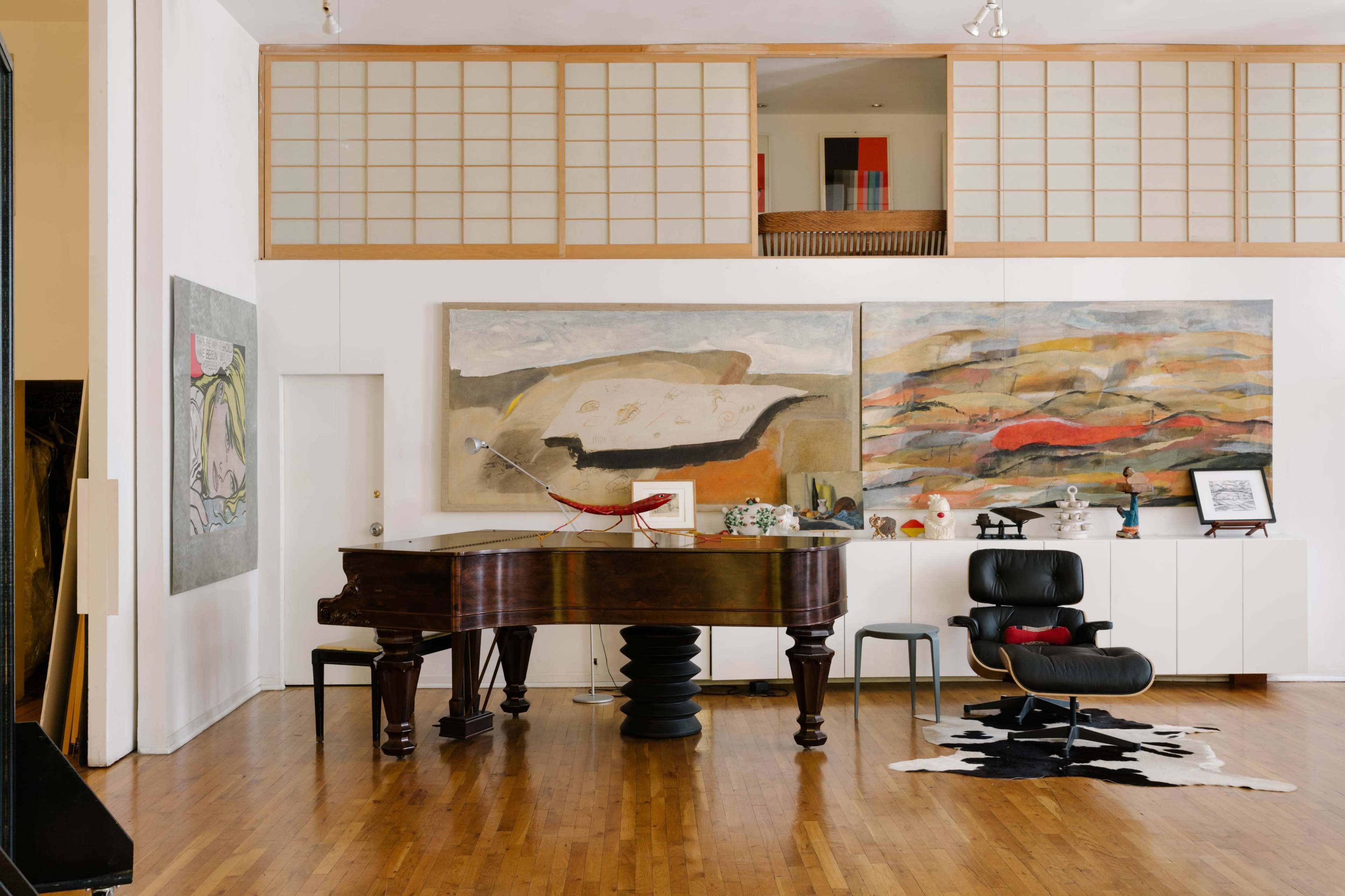 A spacious, well-lit interior showcasing a grand piano, two large abstract paintings on the wall, and modern furnishings including a black chair and a cowhide rug.