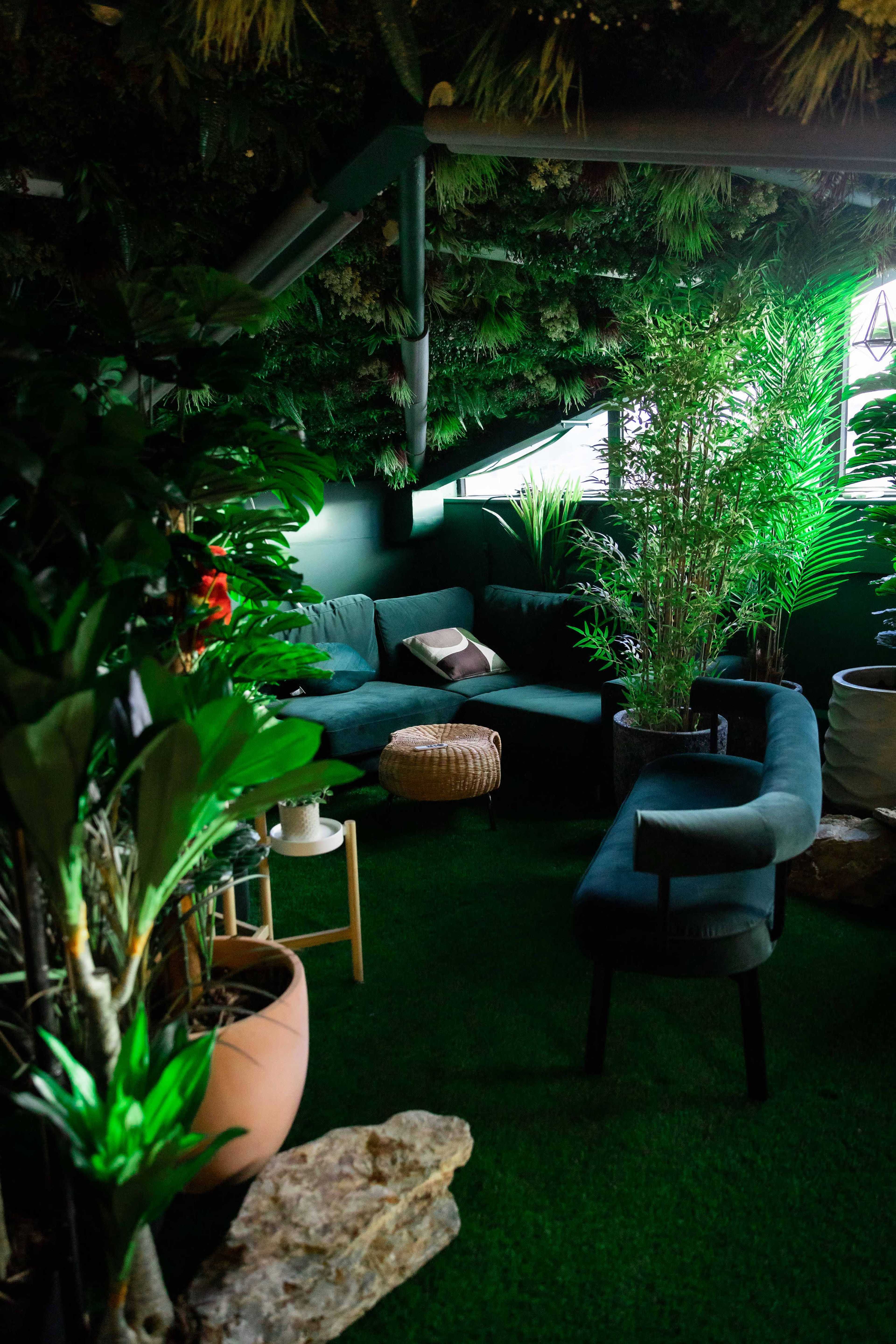 A well-decorated indoor space with a green plant wall, two sofas, and various potted plants on artificial grass flooring.