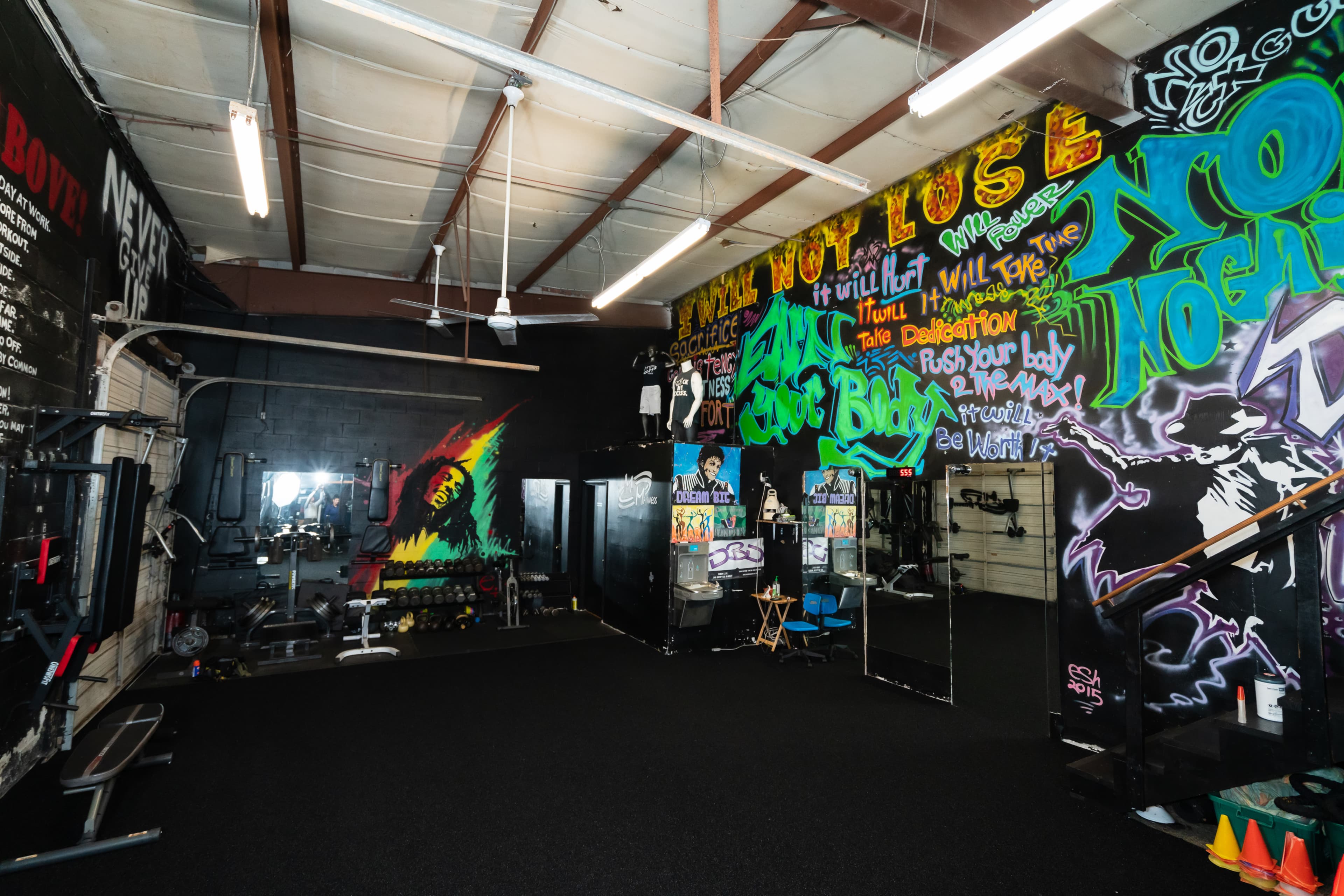 A gym interior with colorful graffiti on the walls, equipment arranged on the floor, and mirrors reflecting the space.