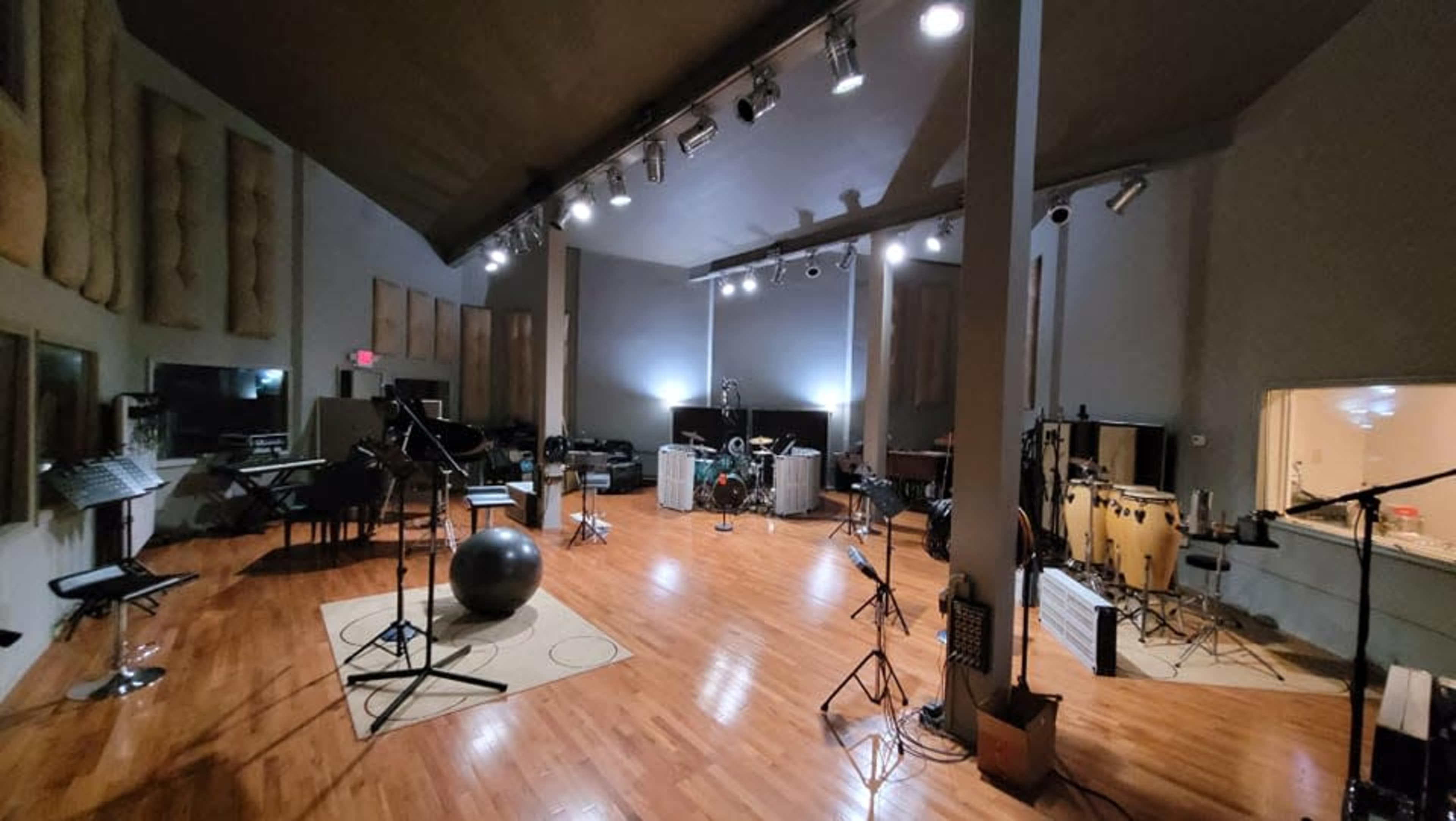 The image shows a large music studio with wooden floors, various musical instruments, and professional recording equipment set up in a spacious room.