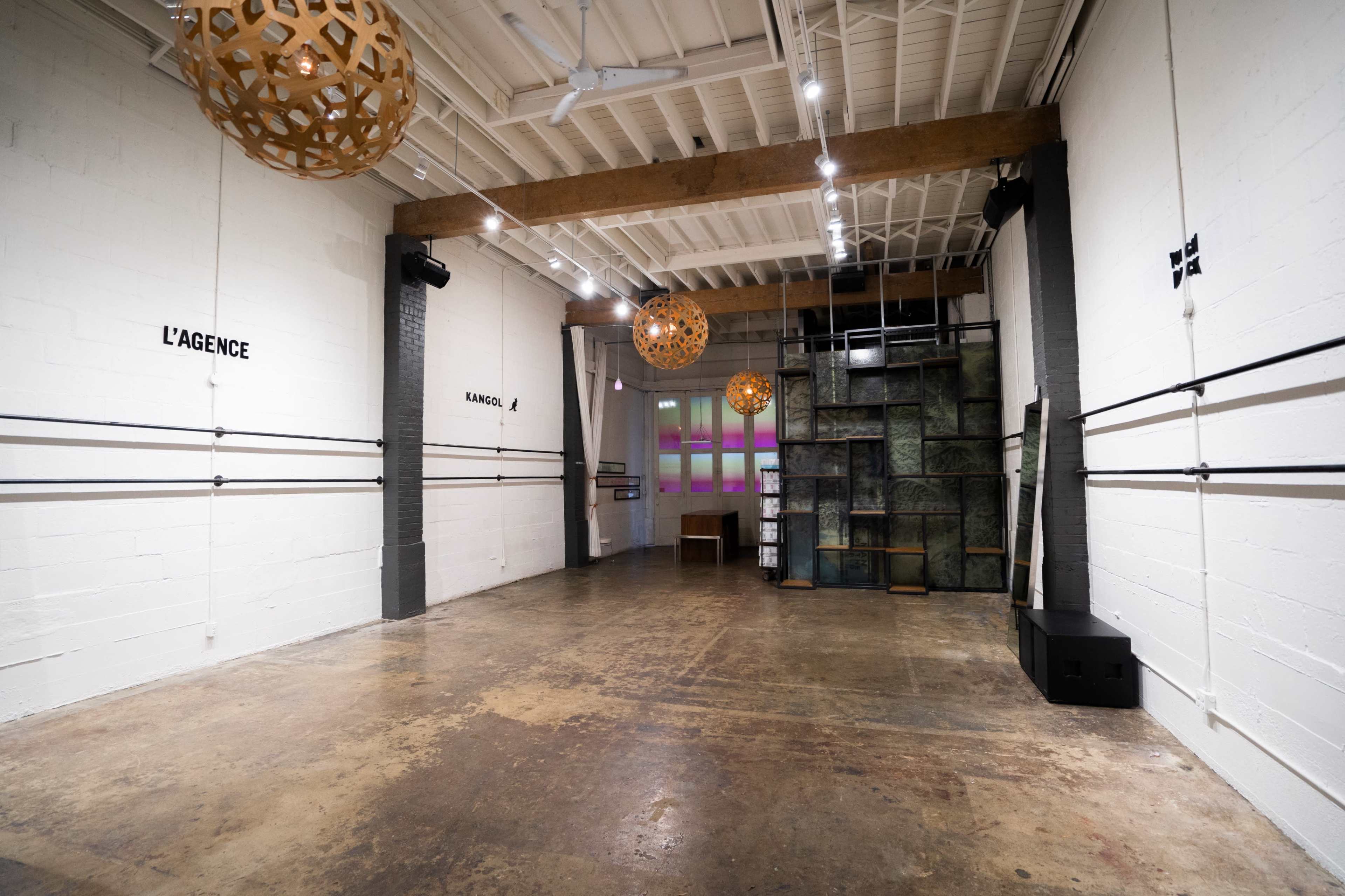 The image shows an empty industrial interior space with wooden beams, concrete walls, and decorative hanging lamps.