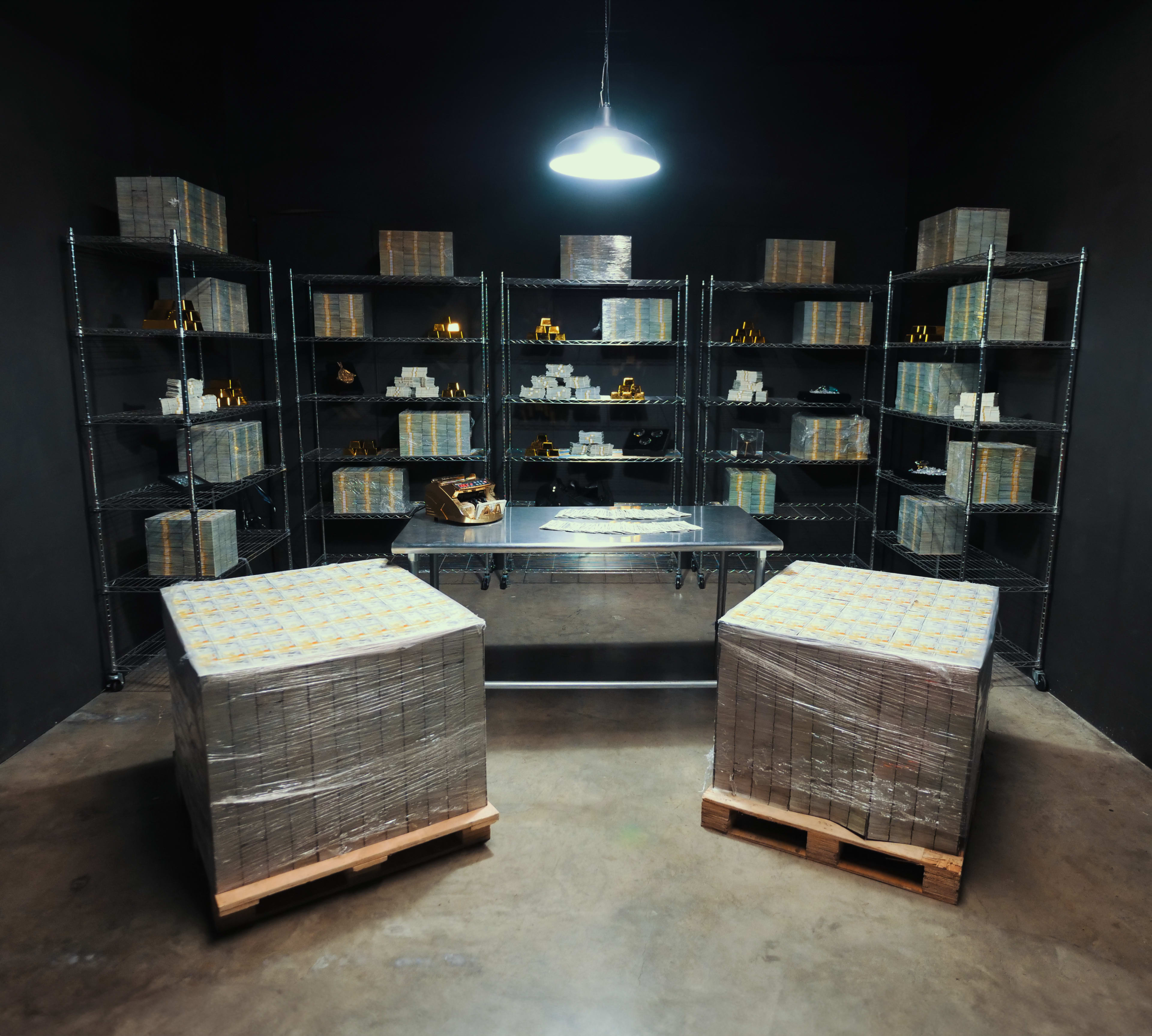 A dimly lit room with metal shelves filled with neatly stacked boxes and a central table surrounded by two pallets of wrapped items.