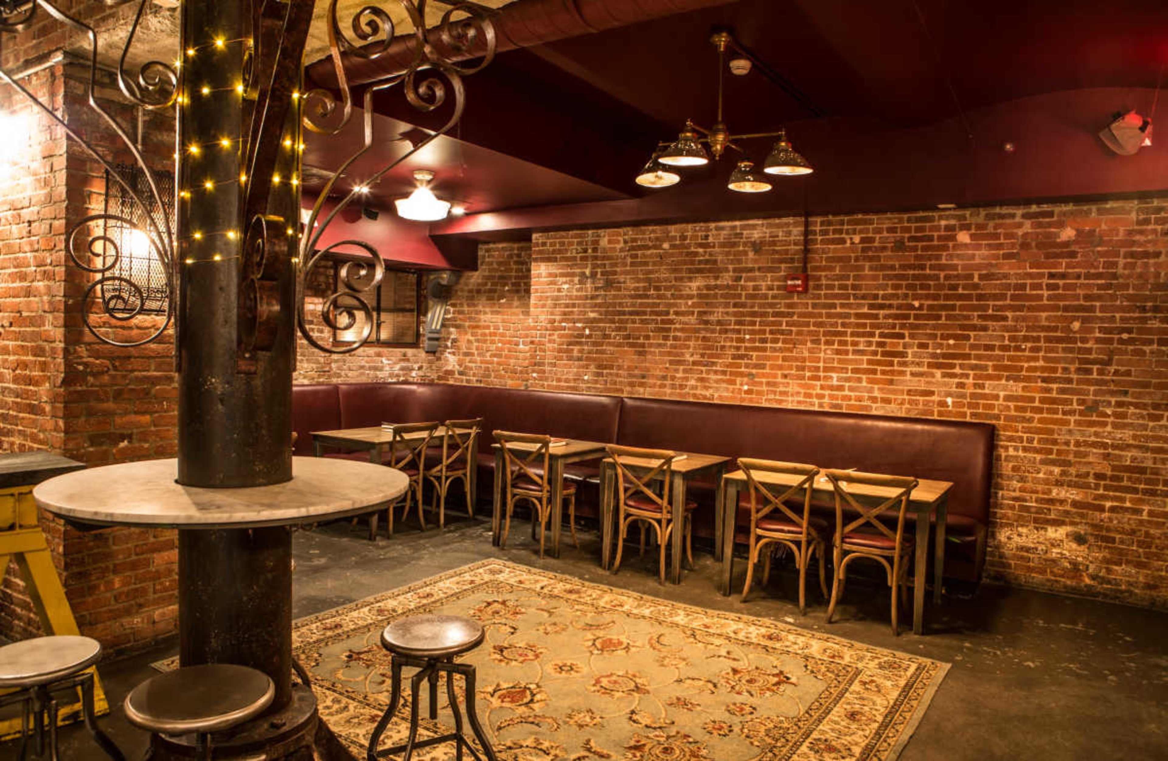The image shows a cozy restaurant interior with exposed brick walls, wooden tables arranged near a plush banquette, and decorative lighting.