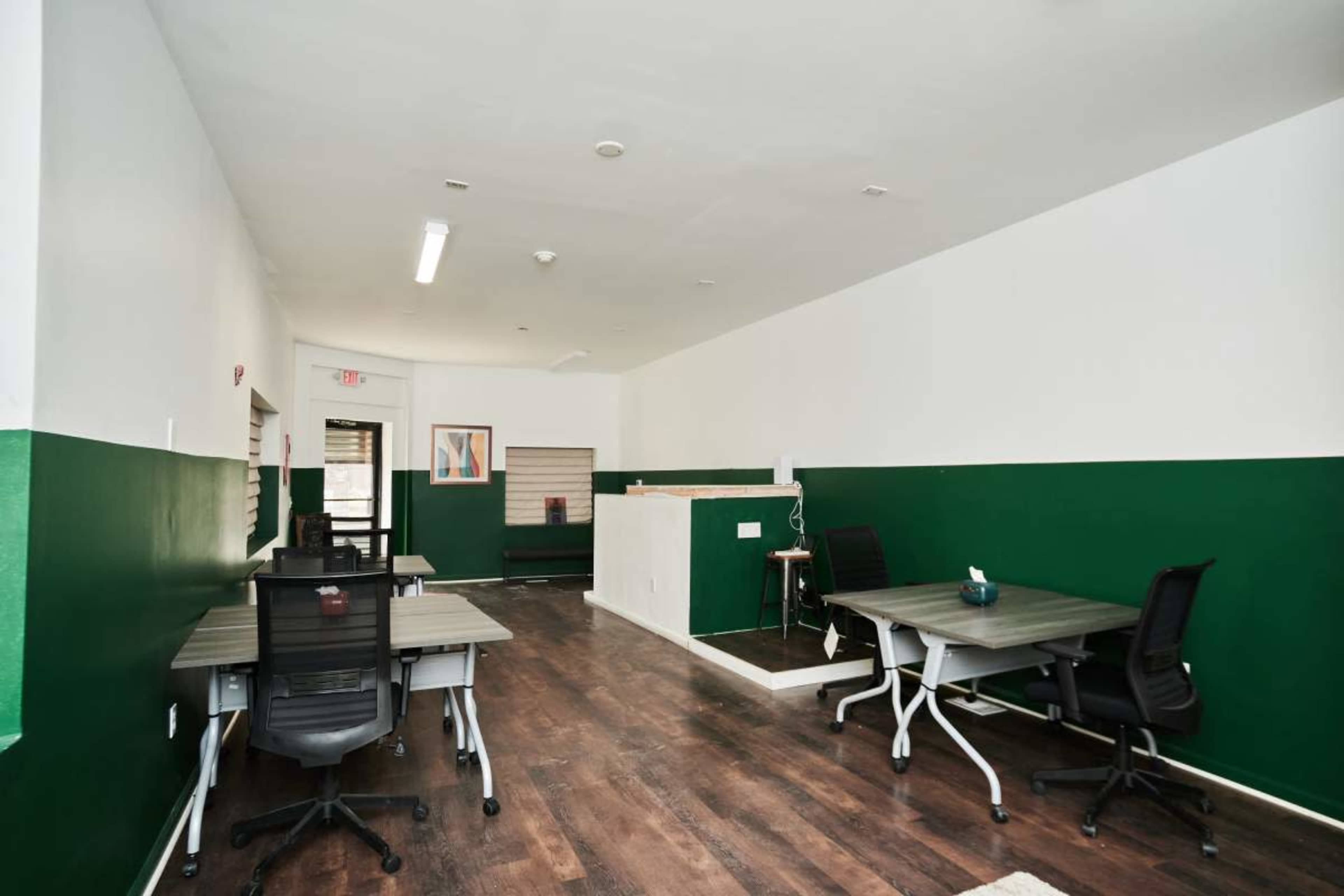A bright office space with green and white walls, featuring several desks and chairs arranged for work.