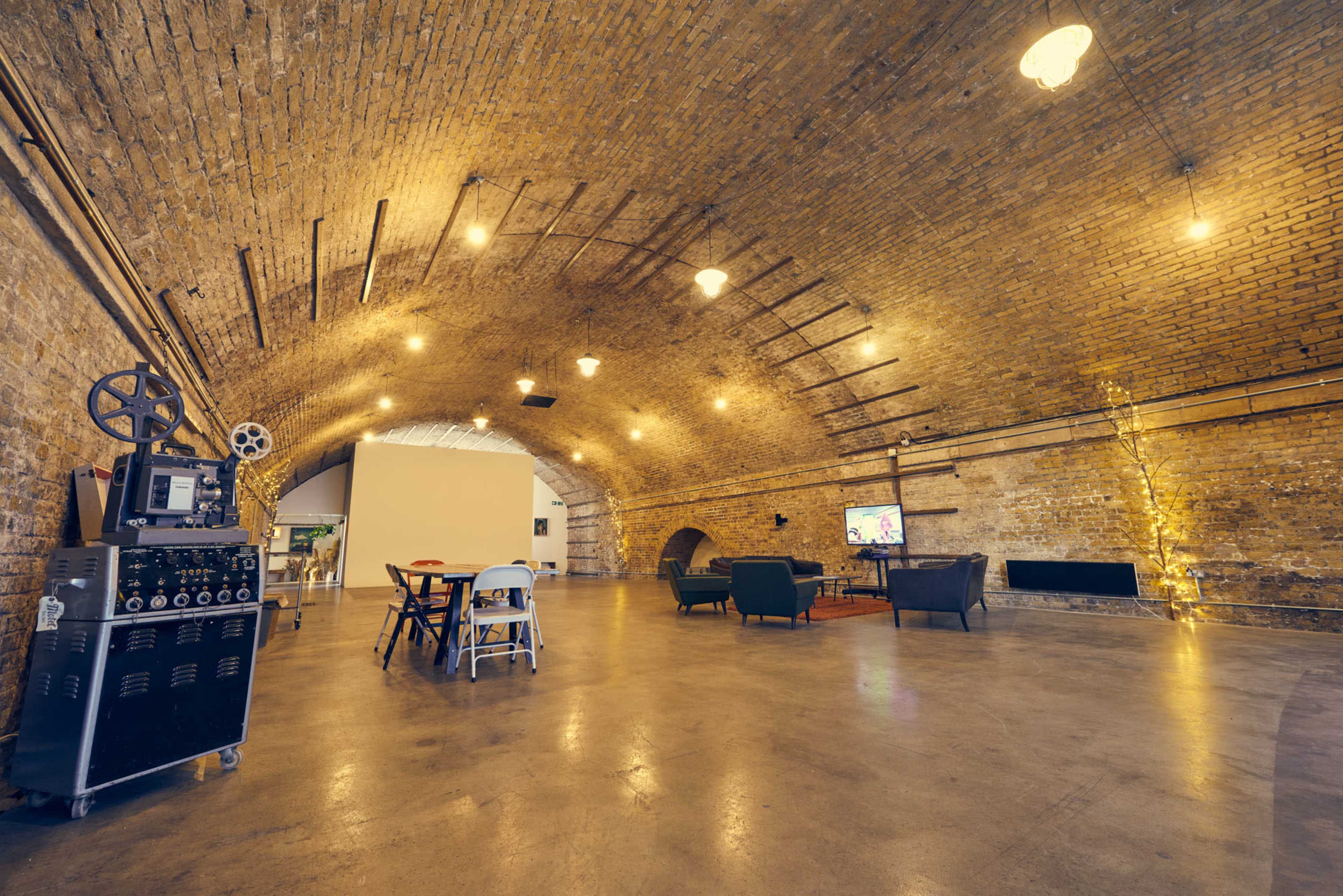 A spacious room with an arched brick ceiling, featuring industrial lighting, wooden furniture, and a decorative TV area.