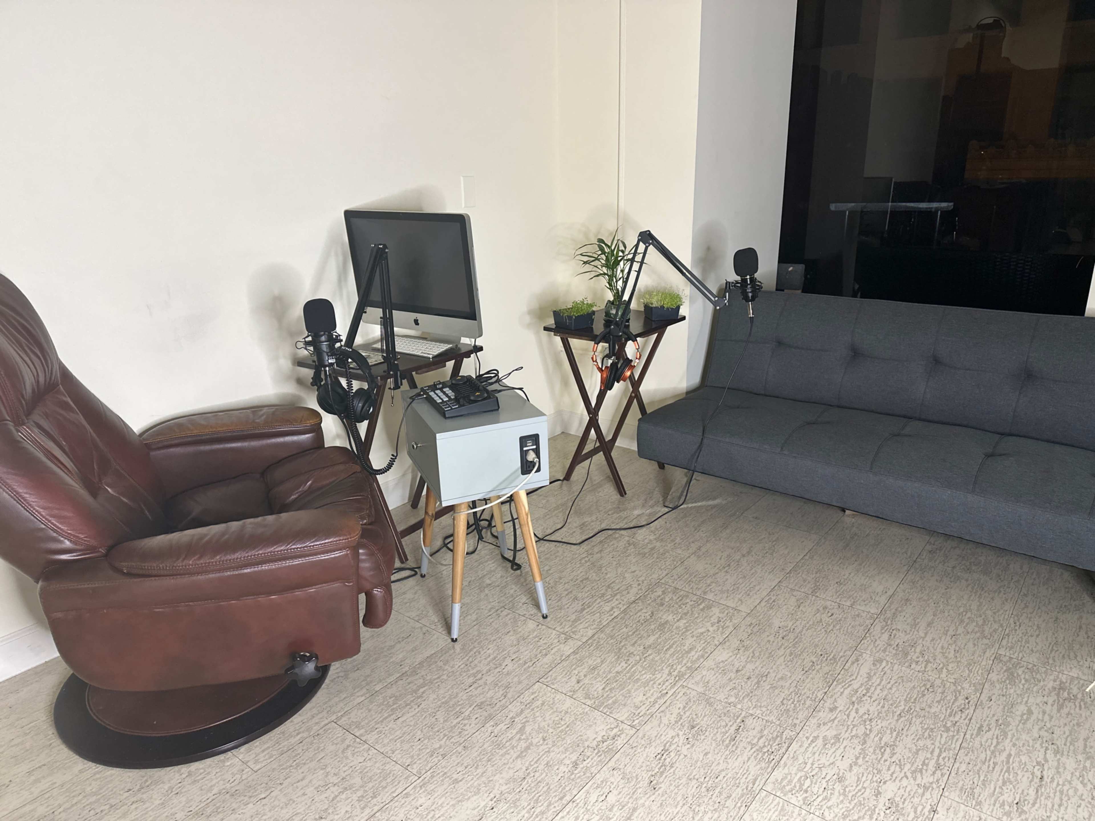 The scene shows a small room with a brown recliner, a gray sofa, a computer with microphones, and a plant on a small table.