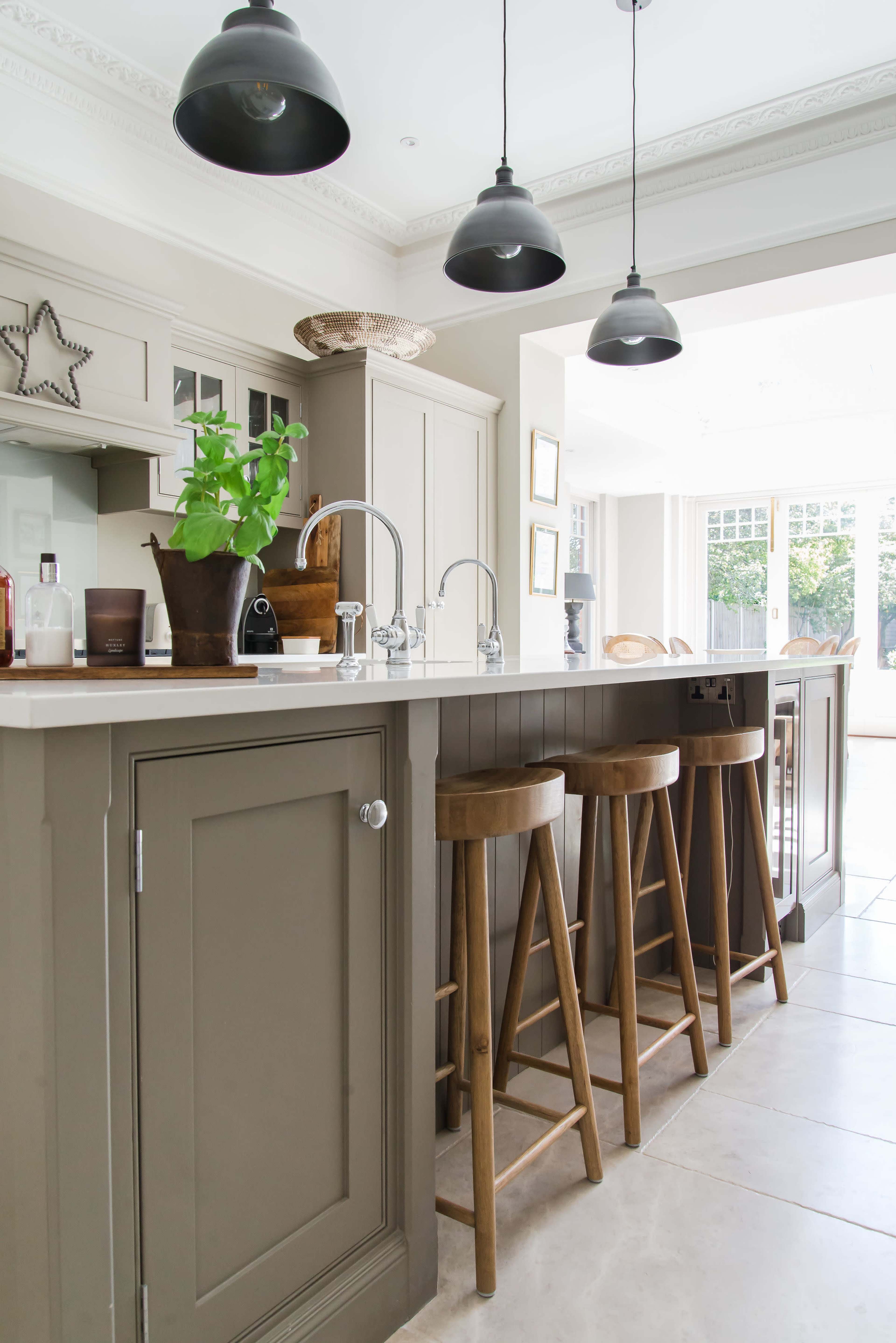 The image shows a modern kitchen with a large island featuring three wooden stools and pendant lighting above.
