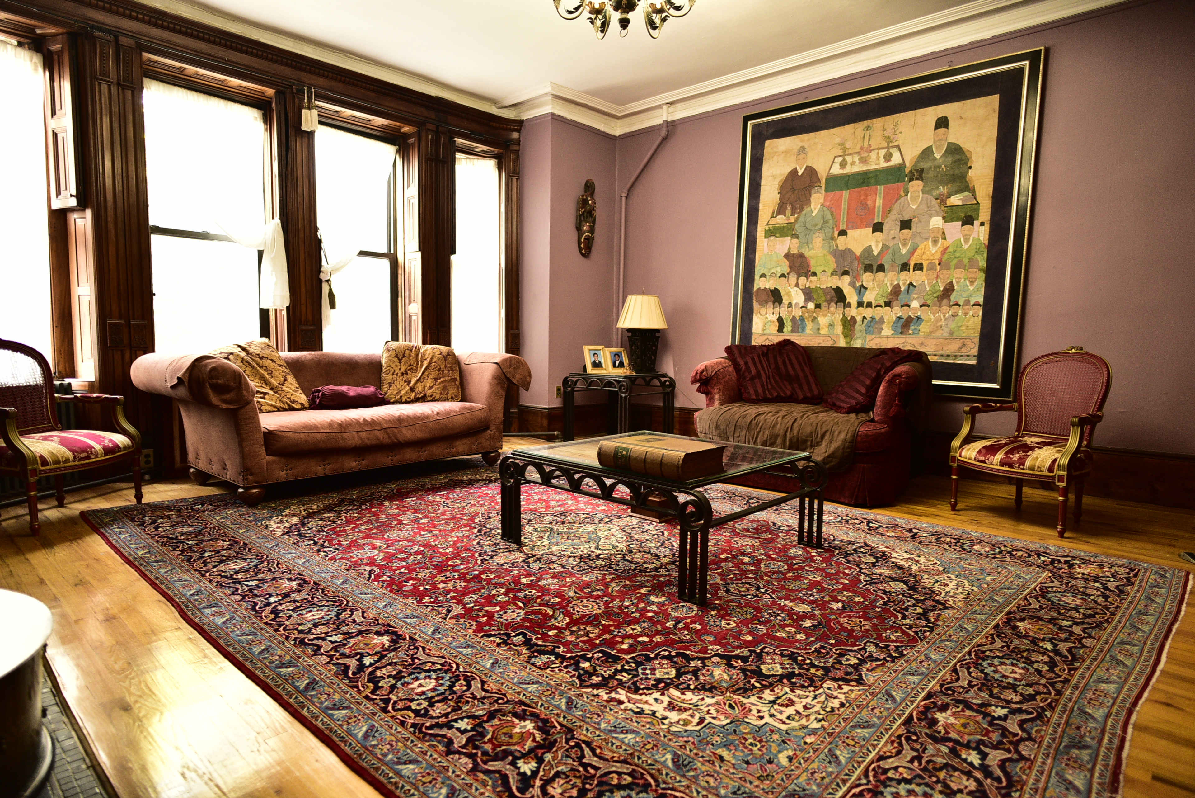 A spacious living room with two sofas, a coffee table, and a large area rug, adorned with artwork on the wall and windows allowing natural light to enter.