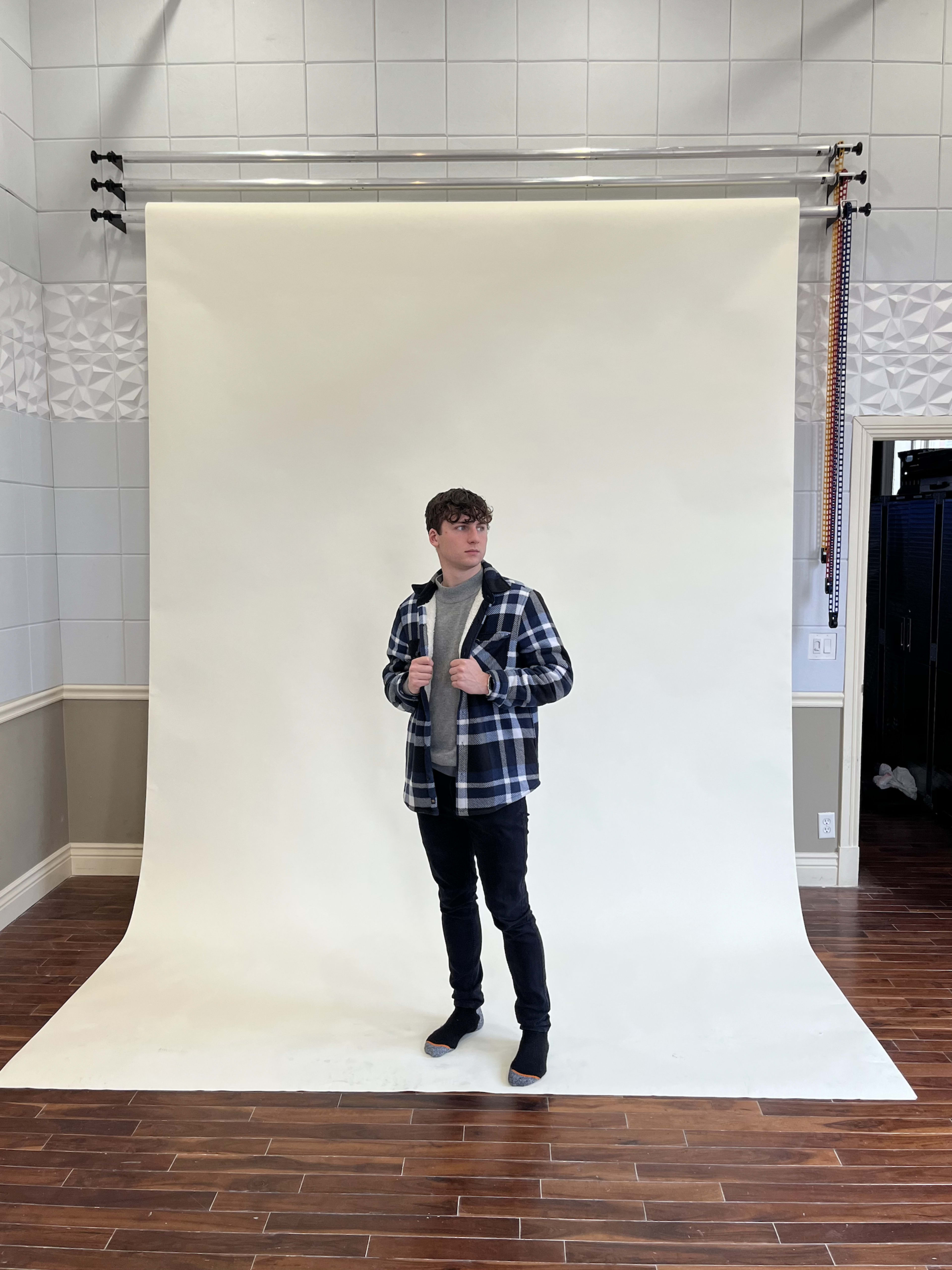 A person in a checkered jacket poses in front of a plain white backdrop in a studio.