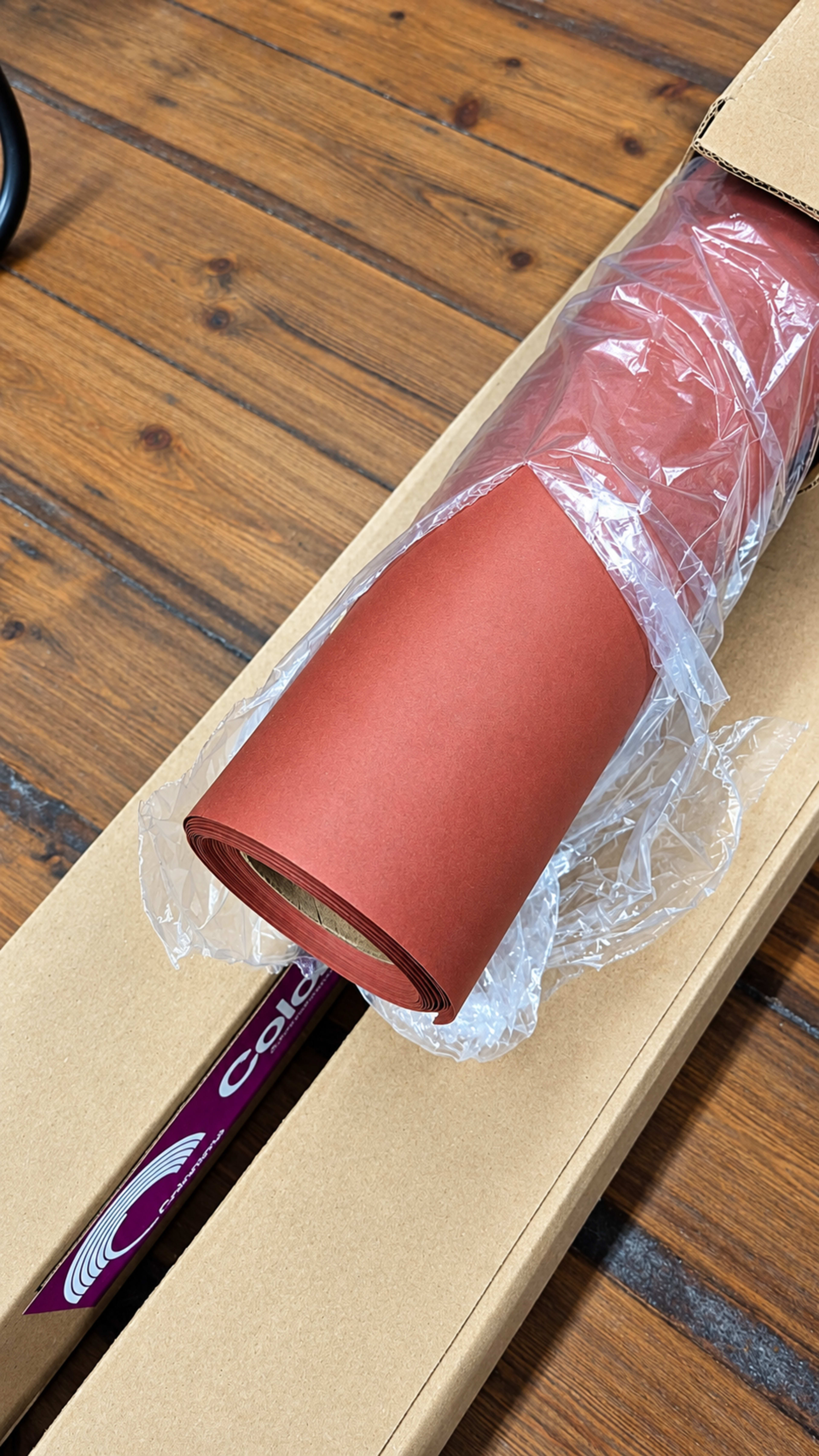 A roll of brown paper is partially unwrapped inside a cardboard box on a wooden surface.