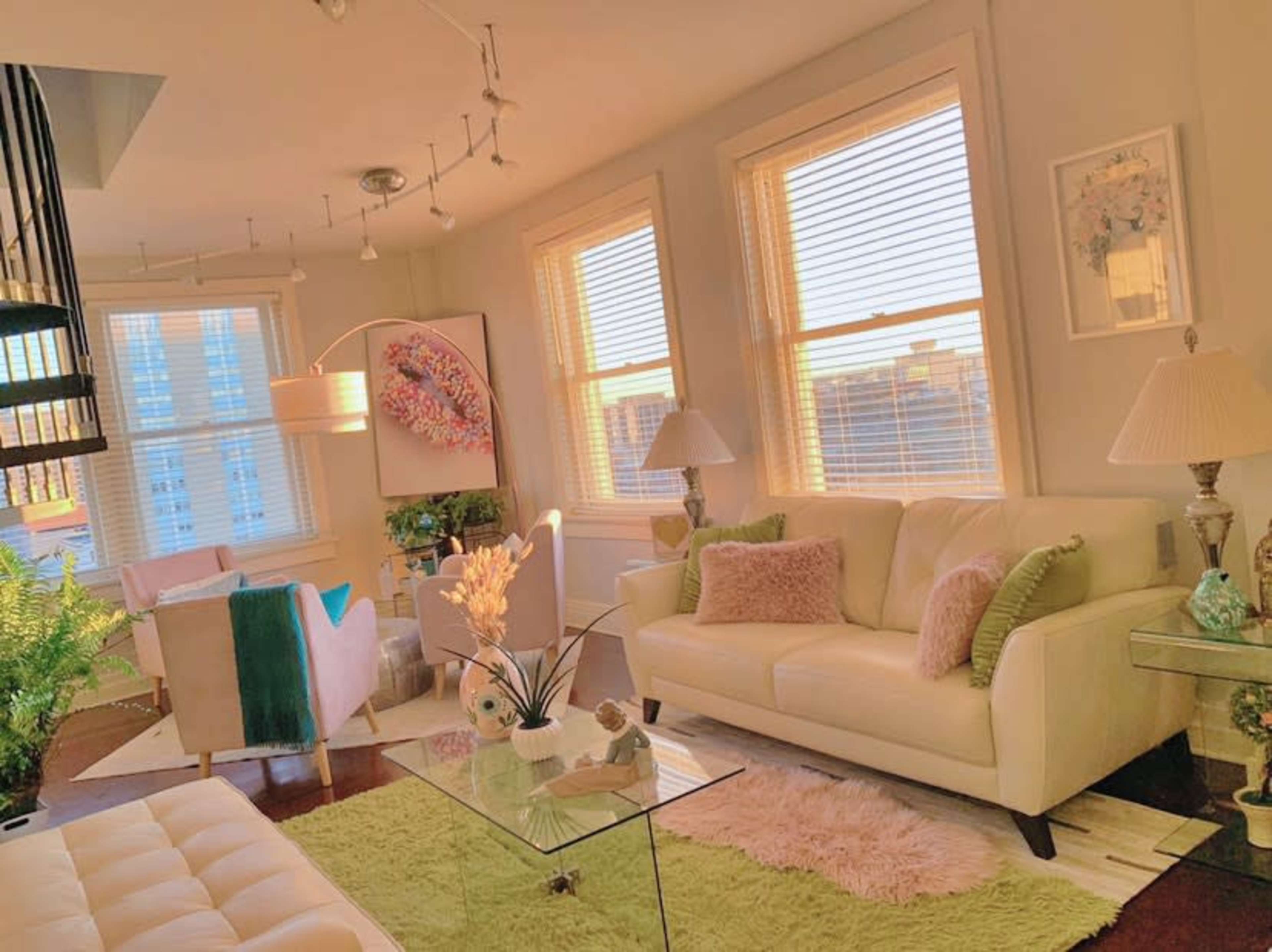 A modern living room features a white couch, glass coffee table, and large windows allowing natural light to fill the space.