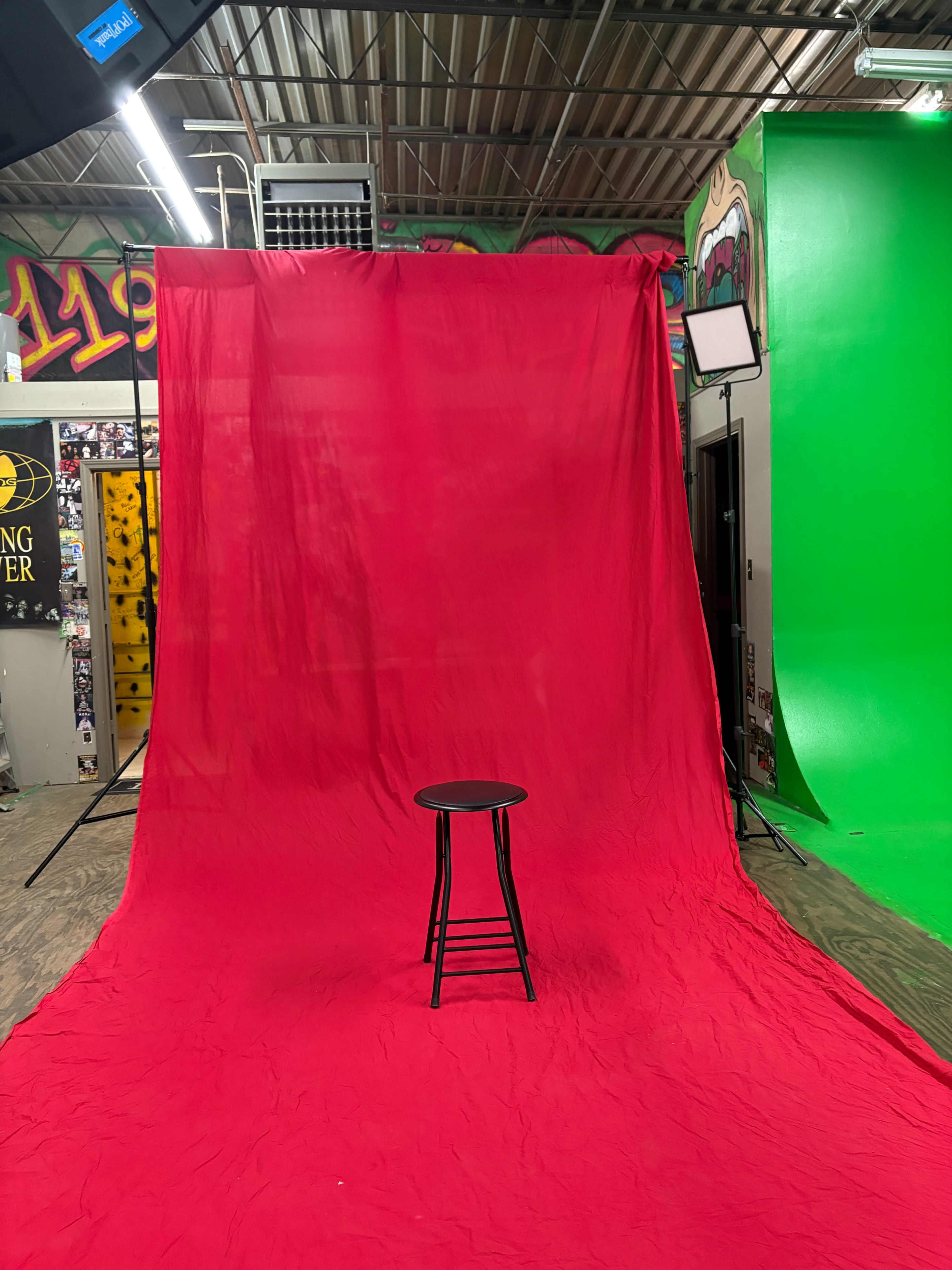 A black stool sits on a red backdrop in a brightly colored studio space.