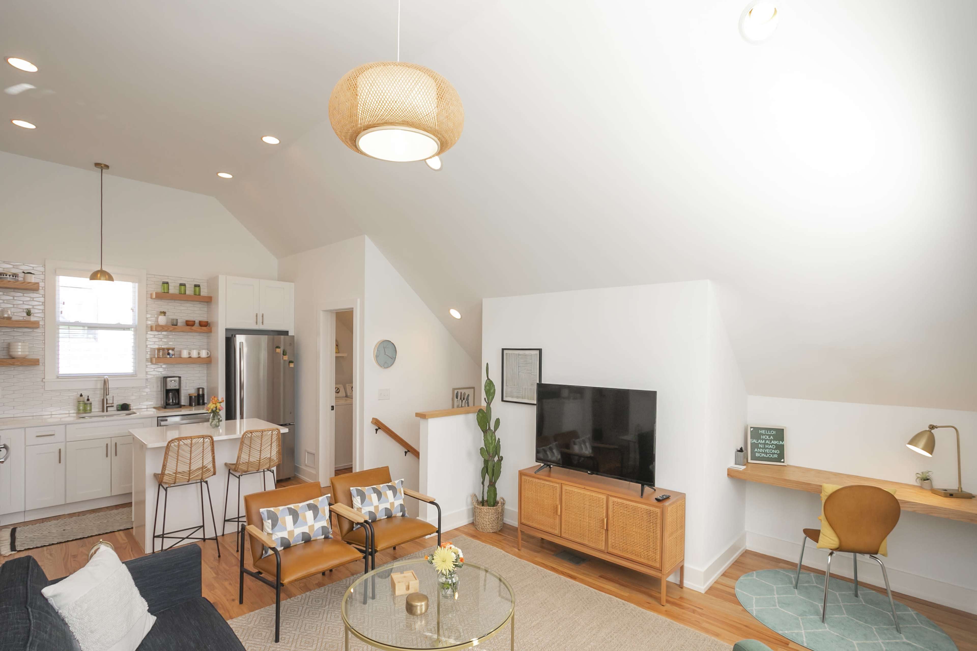 The image shows a modern living space with a kitchen area, a seating area with two chairs, a coffee table, and a television cabinet against the wall.