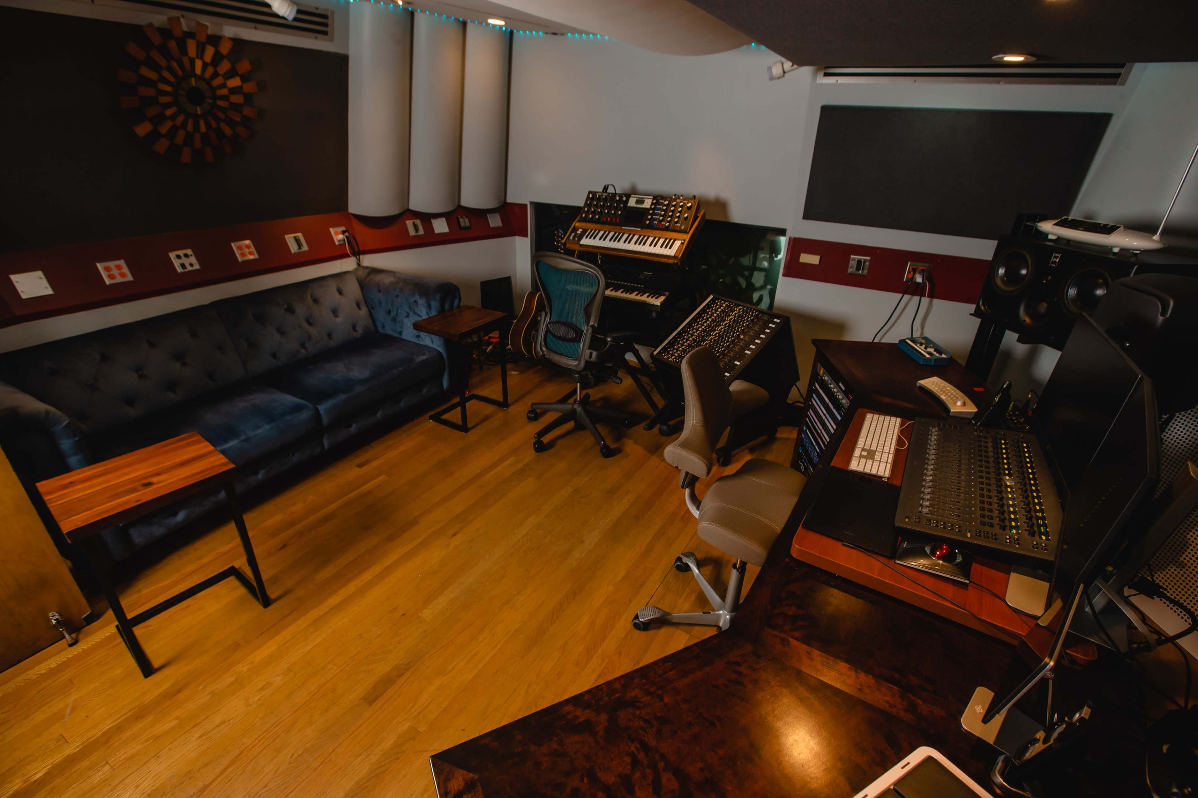 A music studio with a blue sofa, wooden table, and various sound equipment arranged around the room.