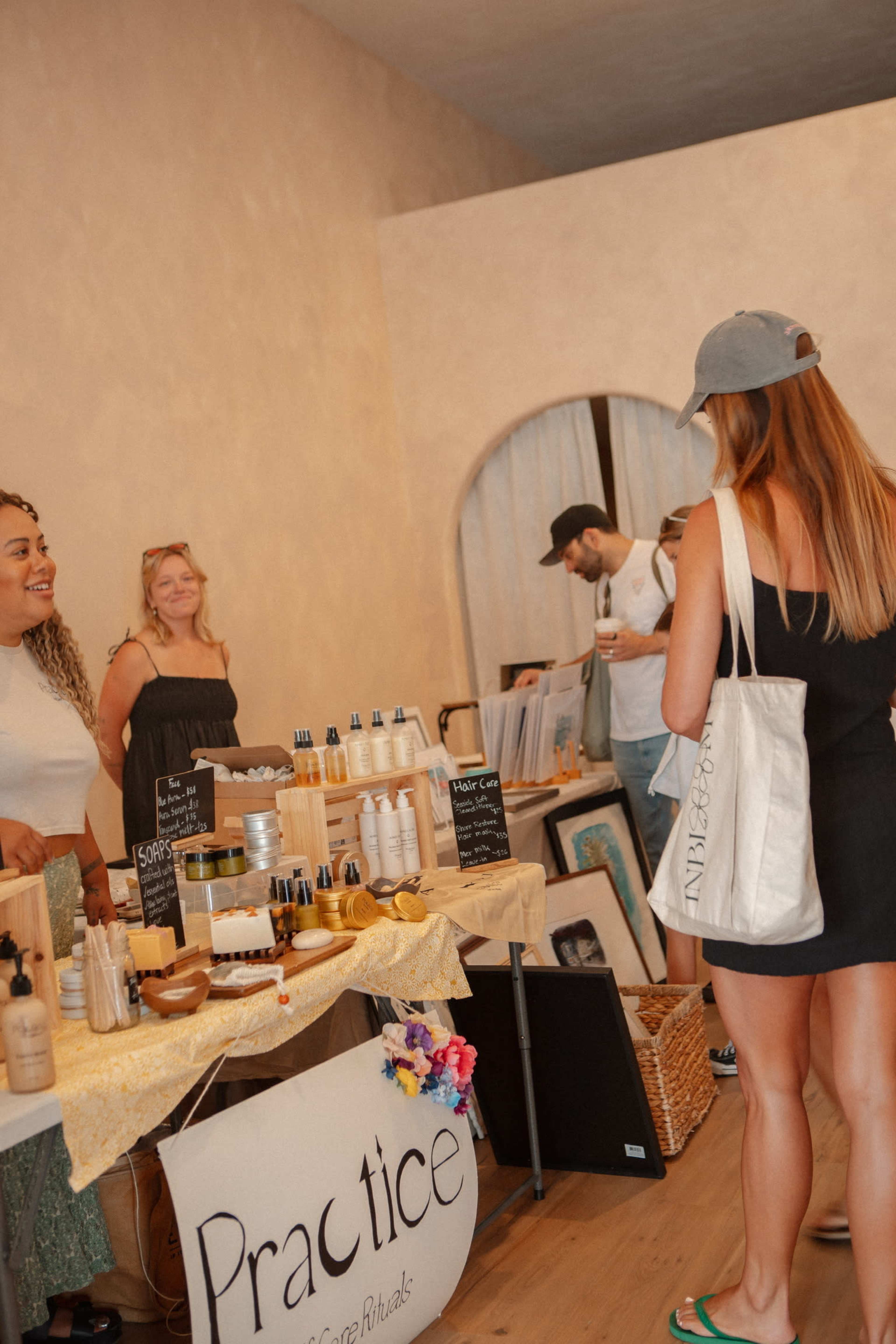 Two women are standing behind a table displaying various beauty products, while a third woman in a black dress interacts with them inside a well-lit shop.