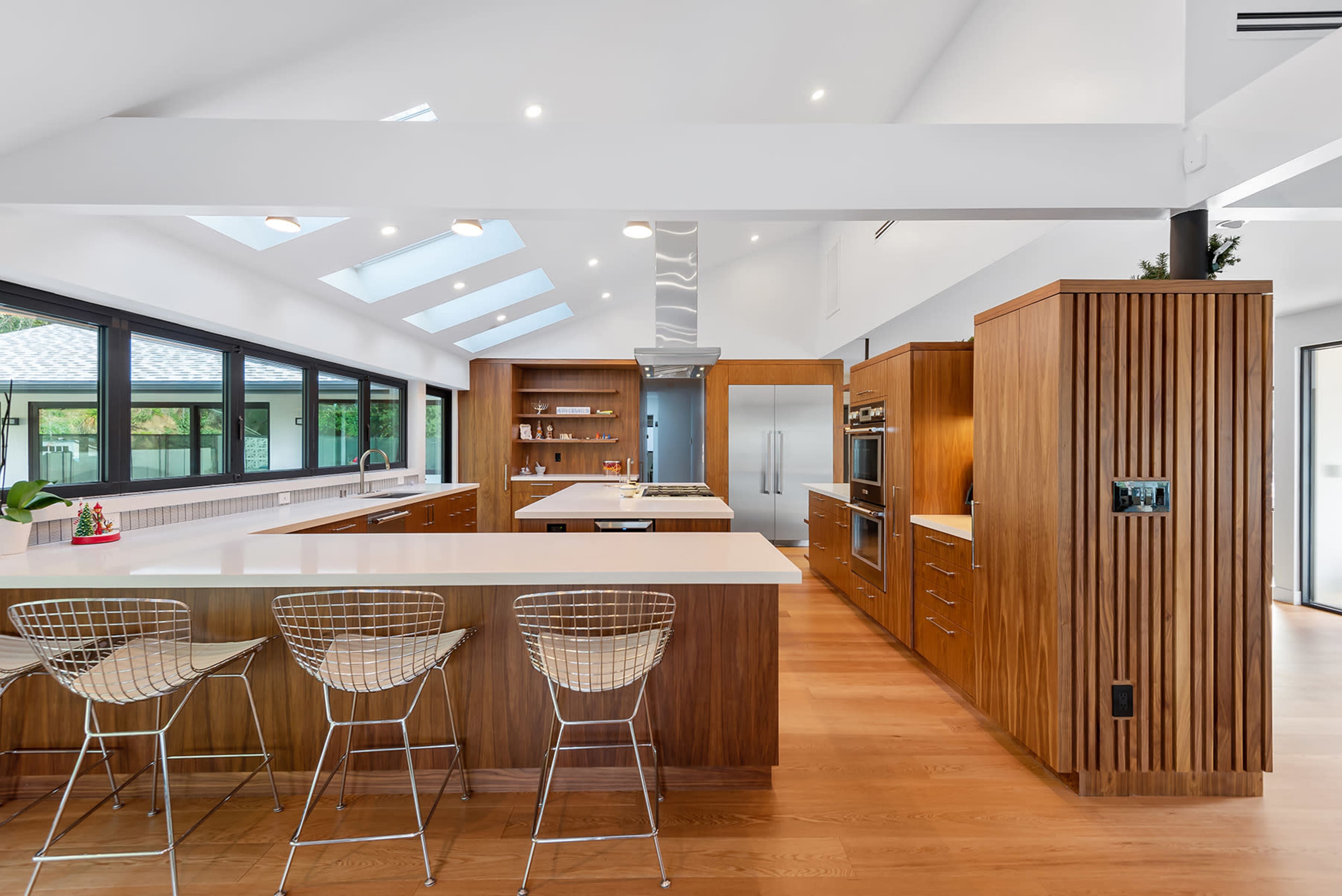 A modern kitchen with wooden cabinetry, an island with bar stools, and skylights illuminating the space.