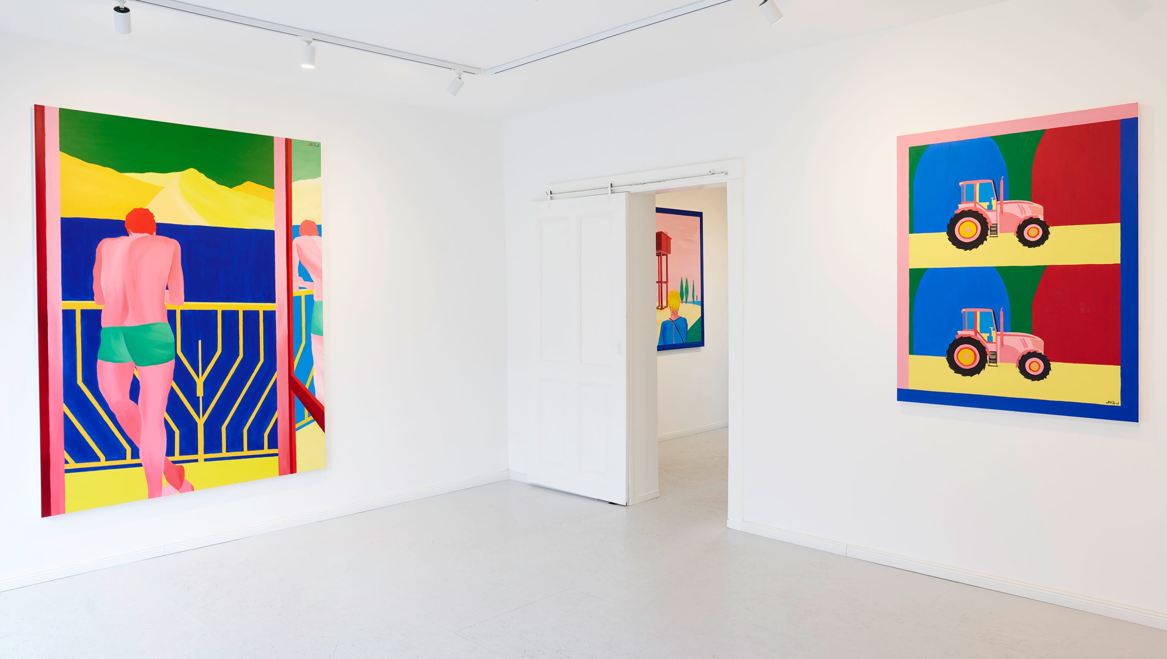 A gallery interior with two colorful paintings on the walls, one depicting a figure by a window and the other featuring tractors.