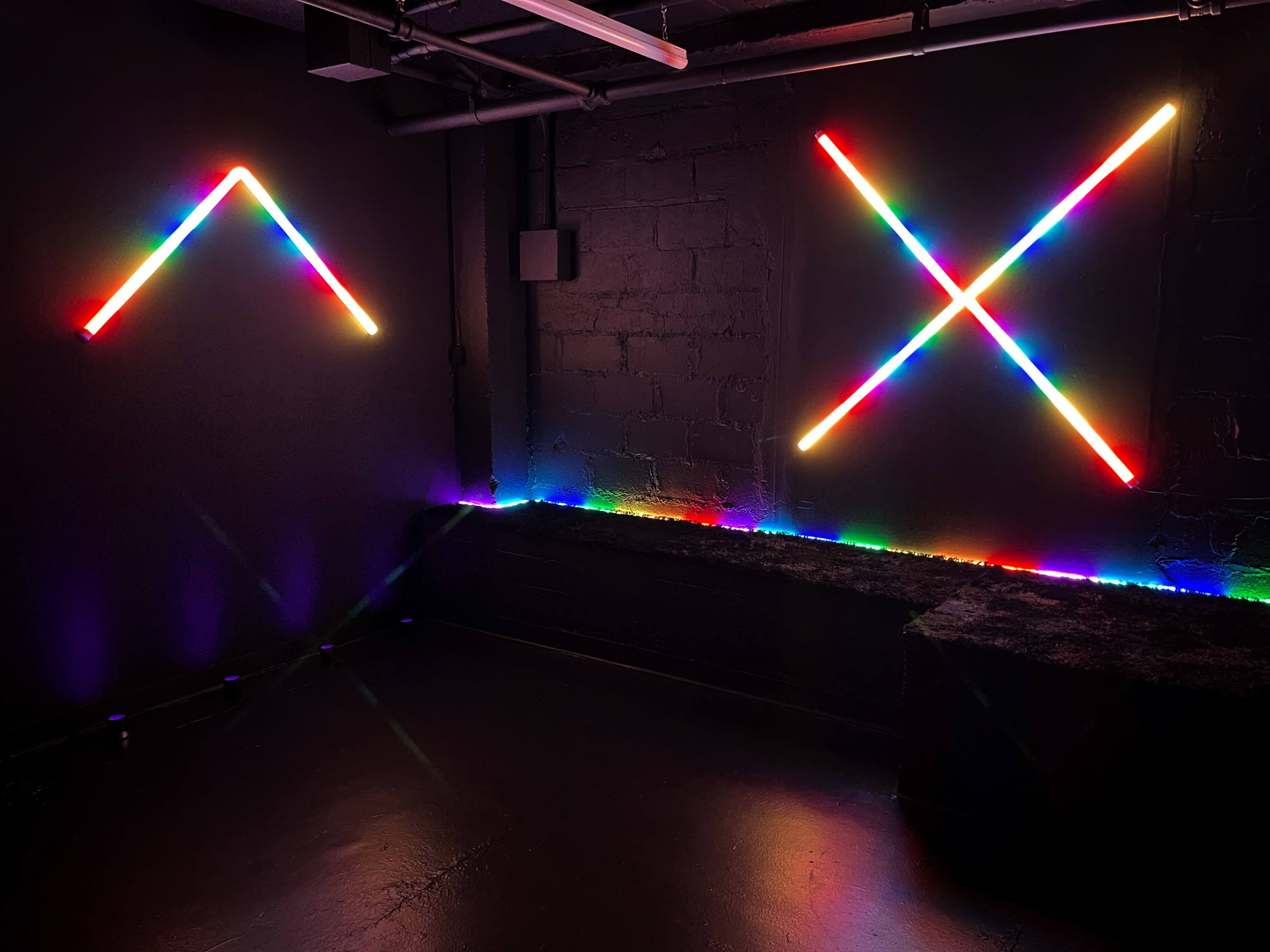A dark room with colorful neon light stripes arranged in geometric shapes on the walls.