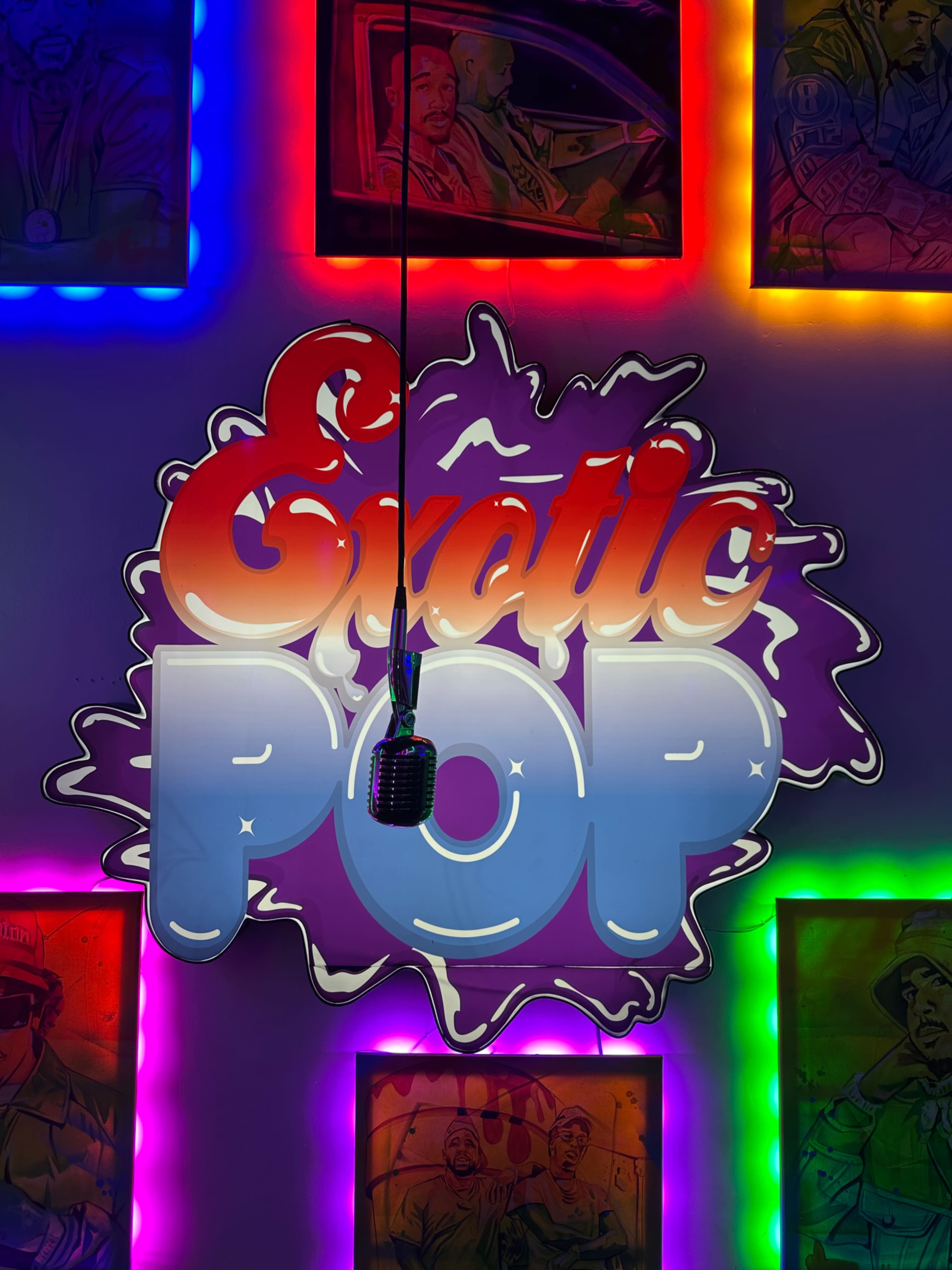 The image features a brightly lit sign that says "Exotic Pop" surrounded by colorful illuminated frames with artwork hanging on a wall.