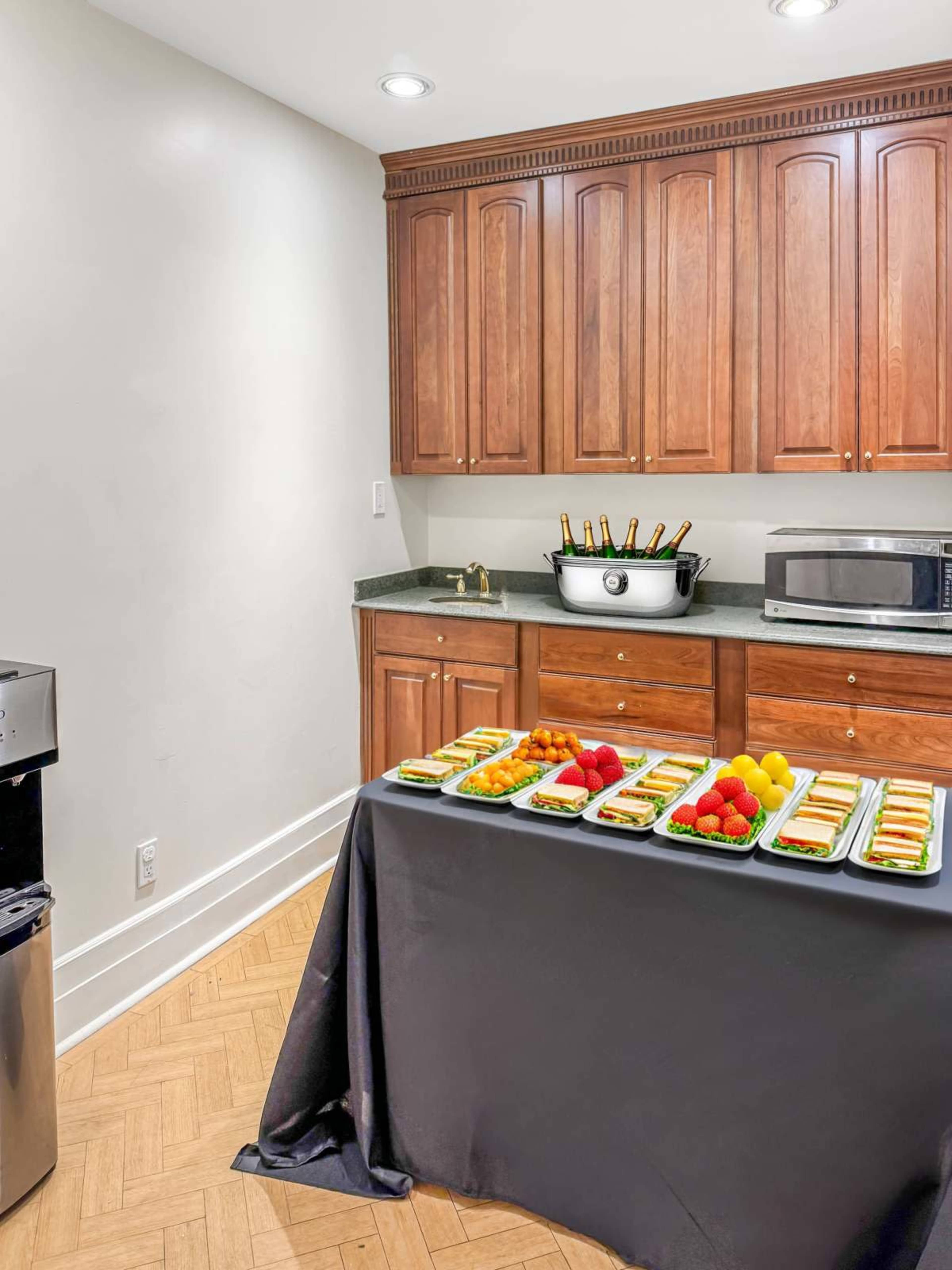 A buffet table is set up in a kitchen area, displaying various food items and four bottles of champagne in a cooler.
