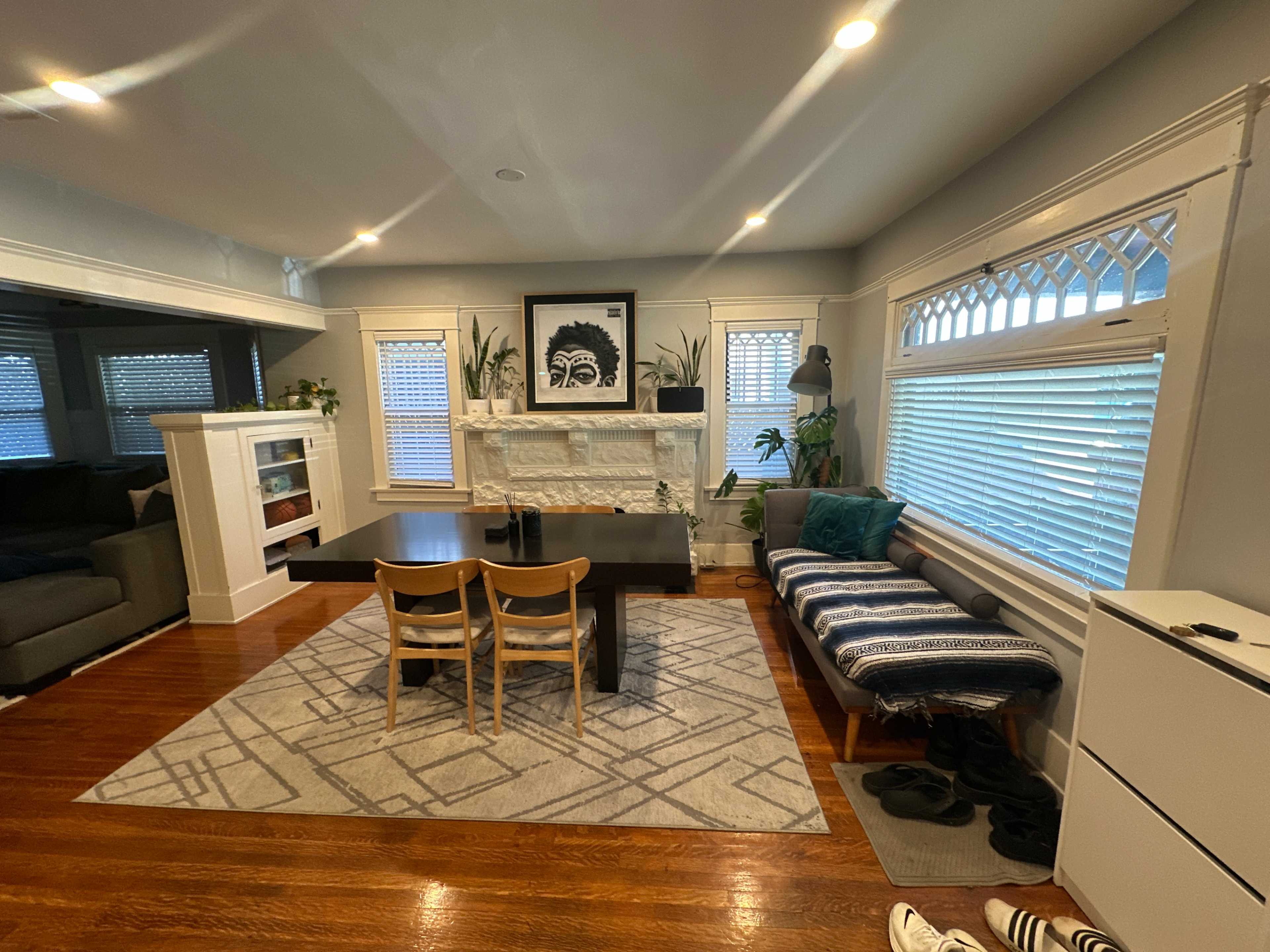 The image shows a cozy dining room with a black dining table, wooden chairs, and a stone fireplace adorned with plants and artwork.