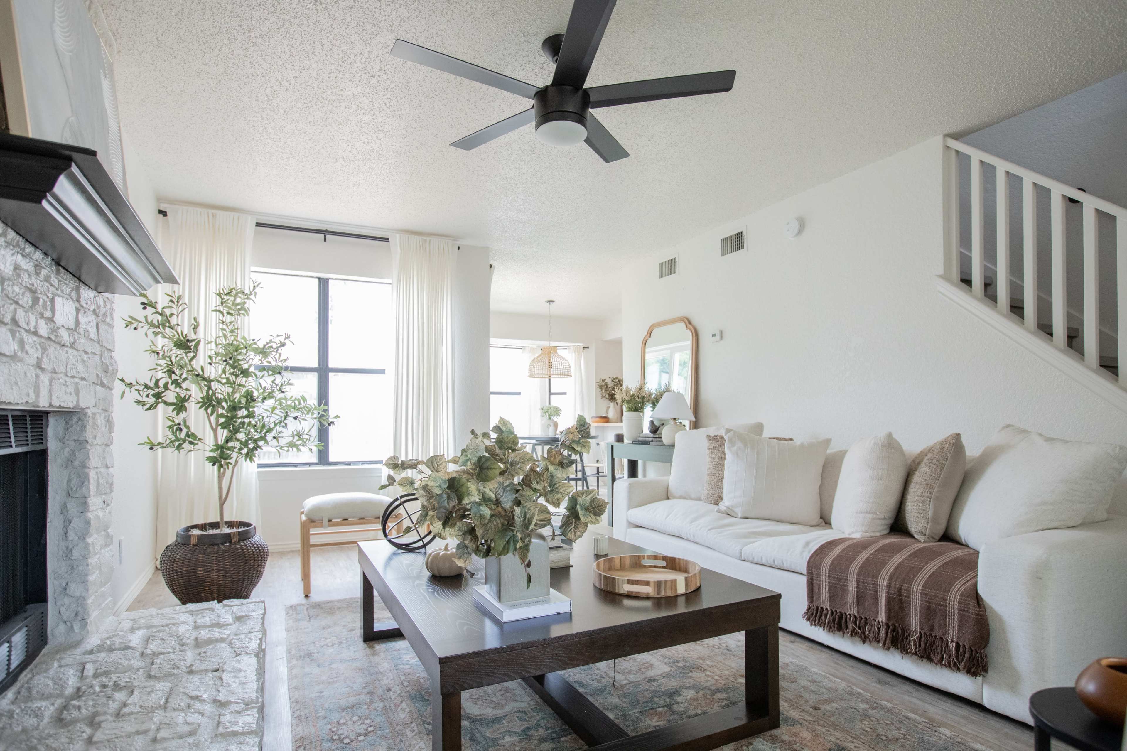 A modern living room with a light-colored sofa, a coffee table, and large windows letting in natural light.