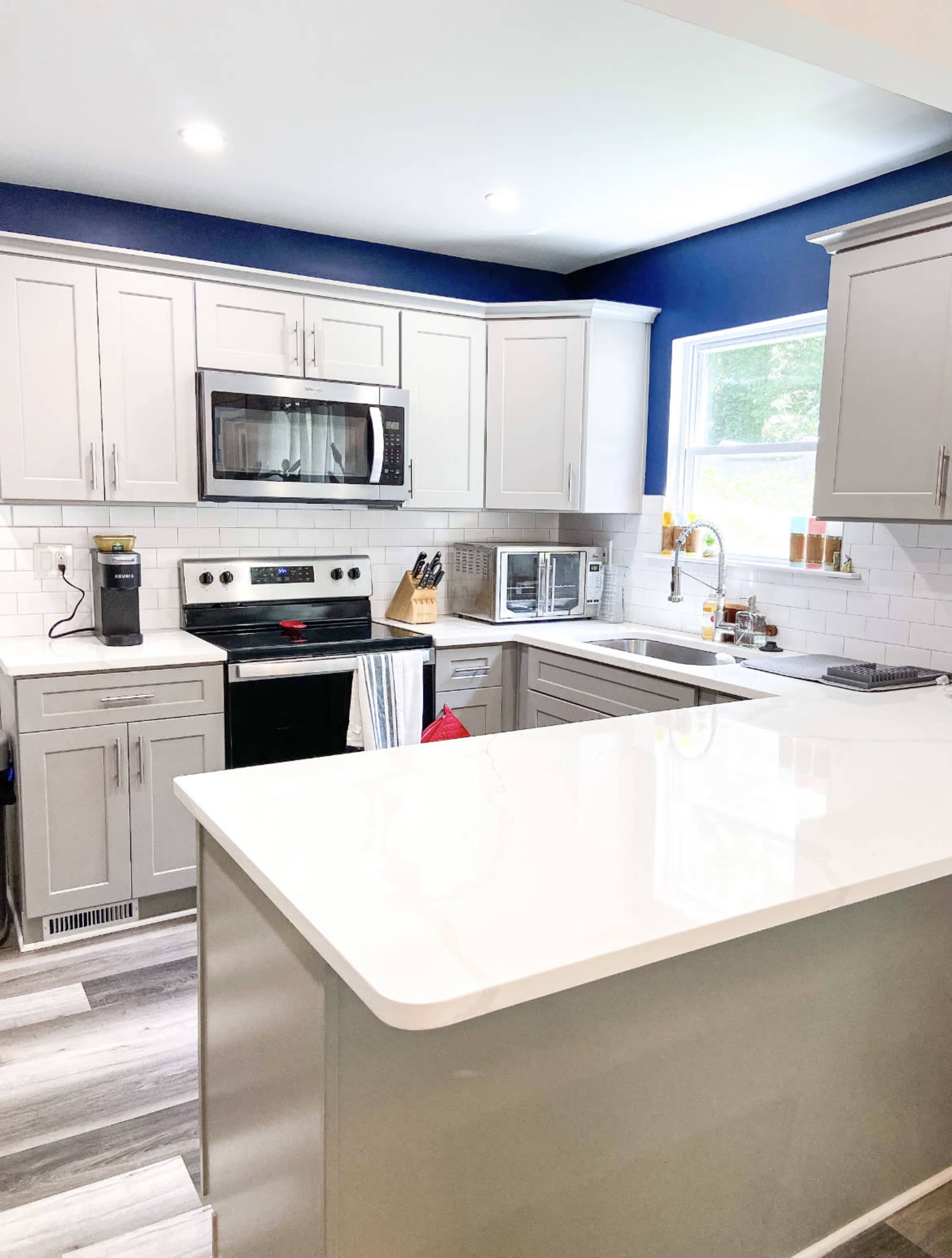 A modern kitchen features gray cabinetry, stainless steel appliances, a white countertop, and a blue accent wall.