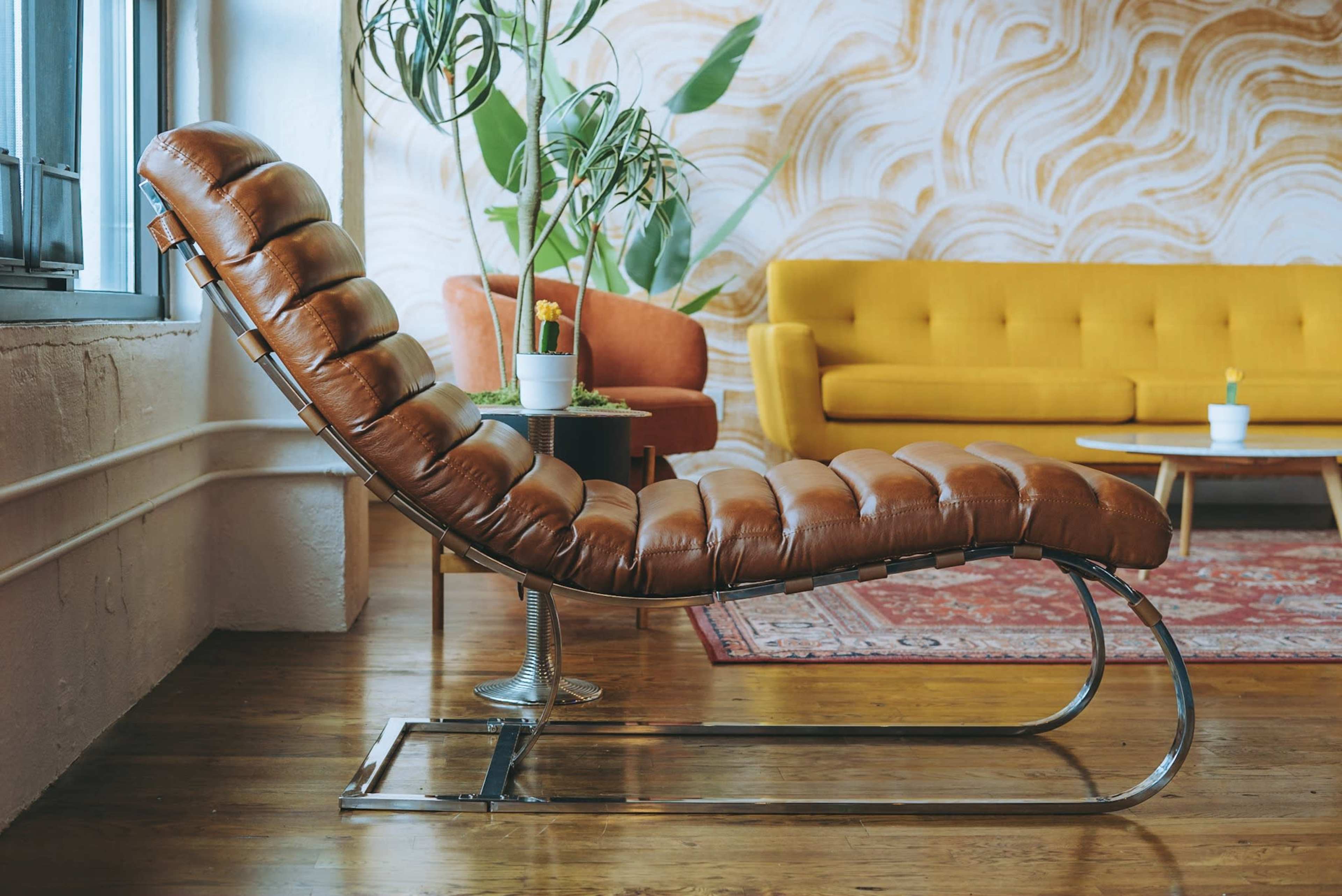 A brown leather chaise lounge is positioned beside a yellow sofa in a room with a patterned wall and wooden flooring.