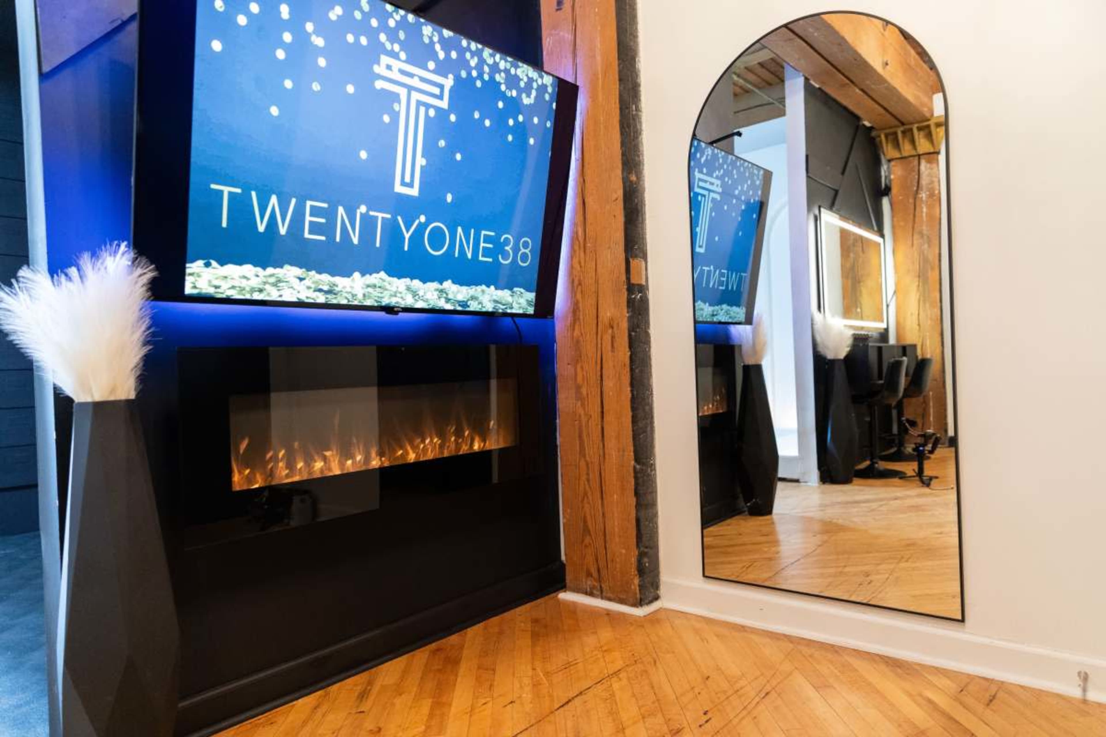 The image features a modern interior space with a large screen displaying the text "TWENTYONE38," a decorative fireplace, and a mirror reflecting the surroundings.