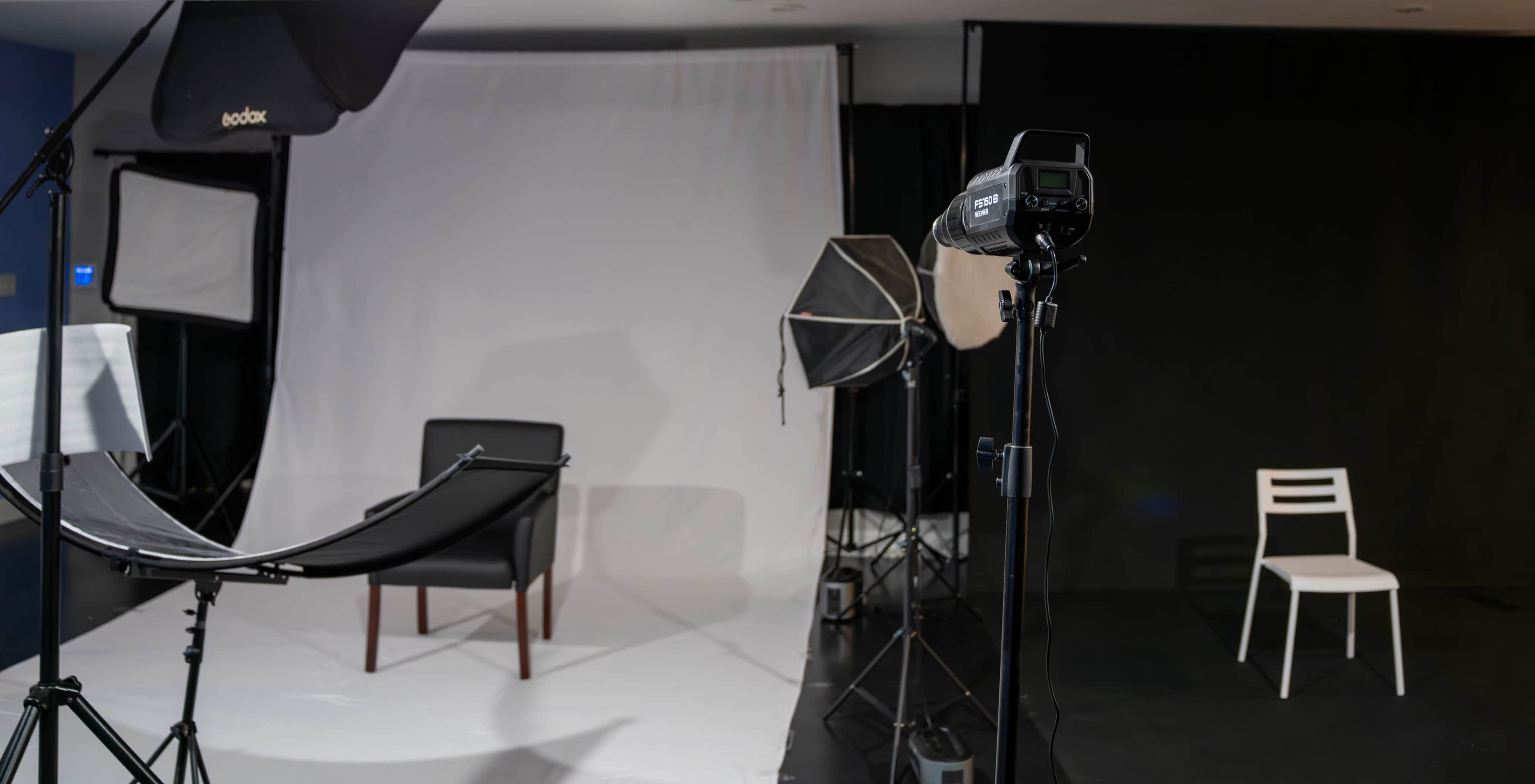 A photography studio setup with a black chair, softboxes, and a white backdrop.