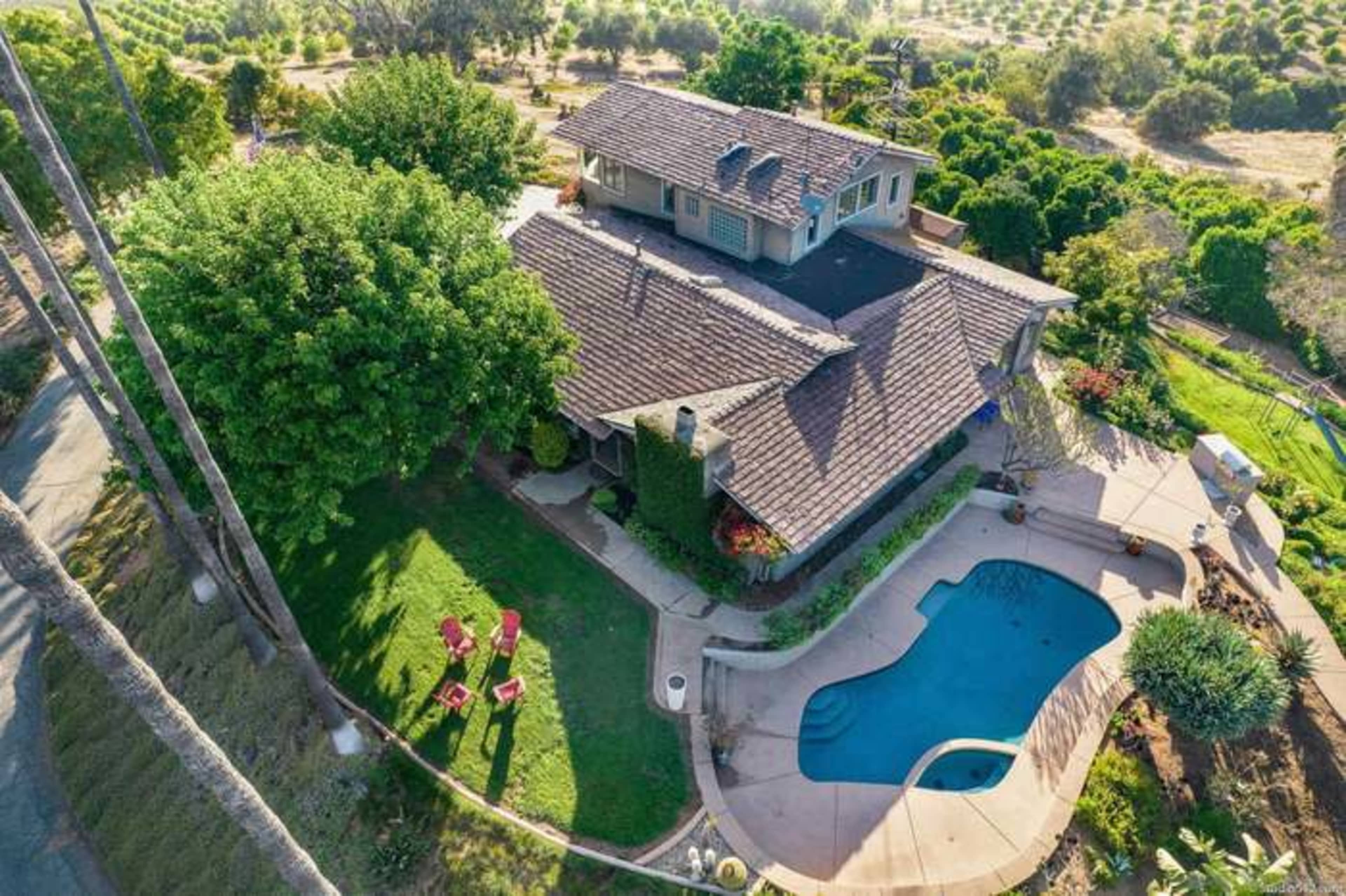A two-story house with a pool and lounge chairs, surrounded by lush greenery and trees.