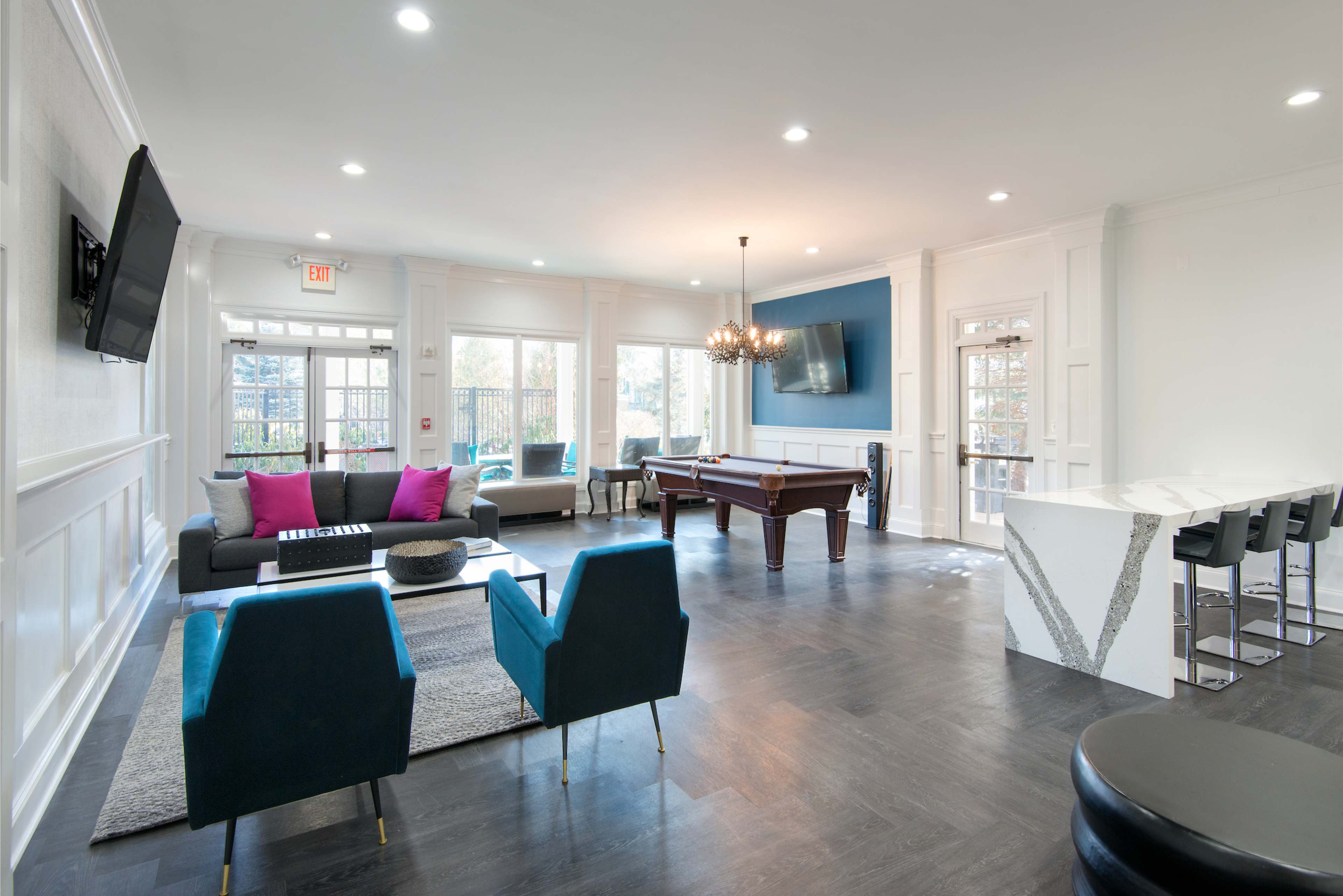 A modern lounge area featuring a pool table, a sectional sofa with pink and gray cushions, and a bar with high stools.