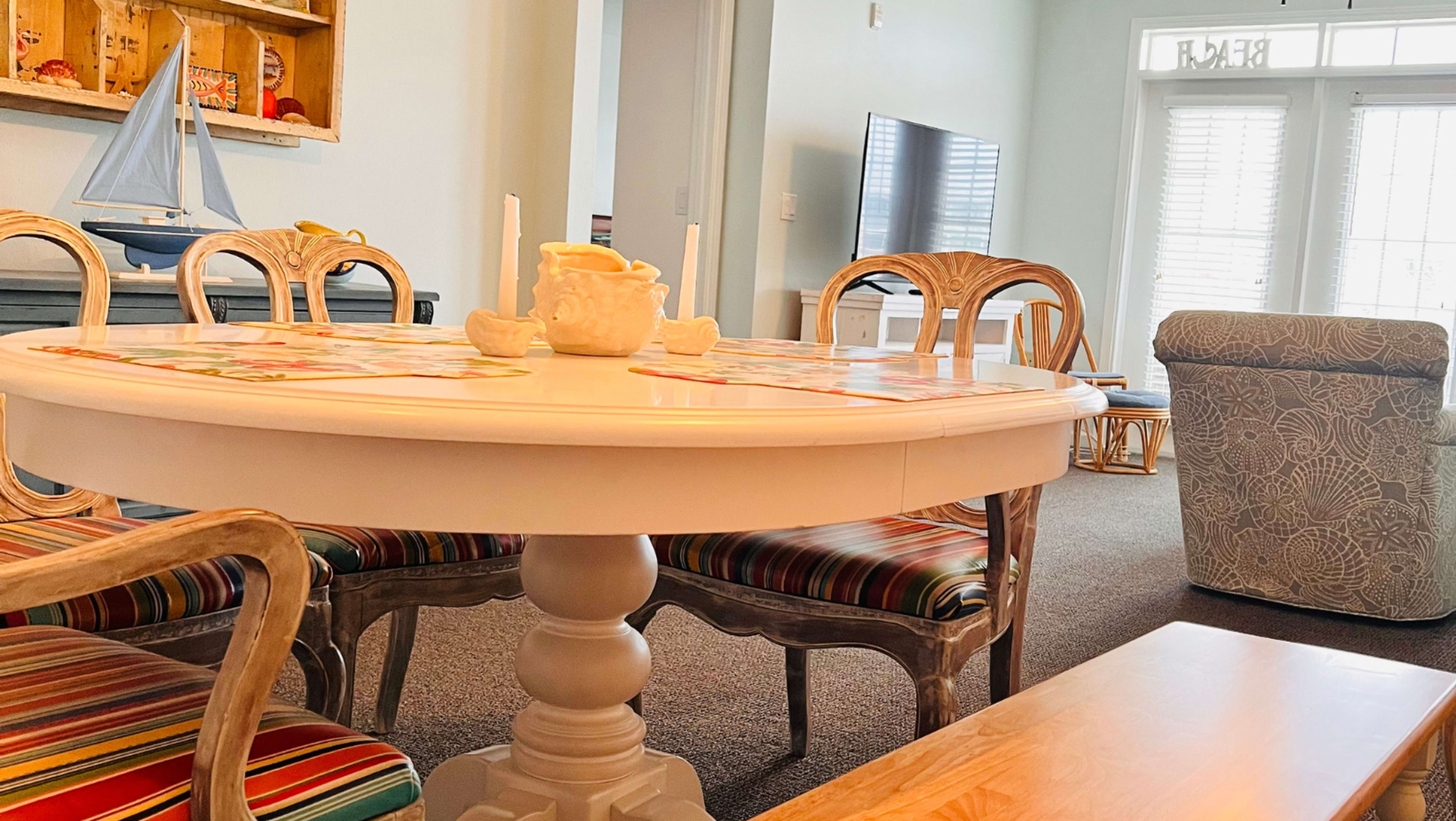 A round dining table with striped chairs is set in a bright living space featuring a couch and a television.