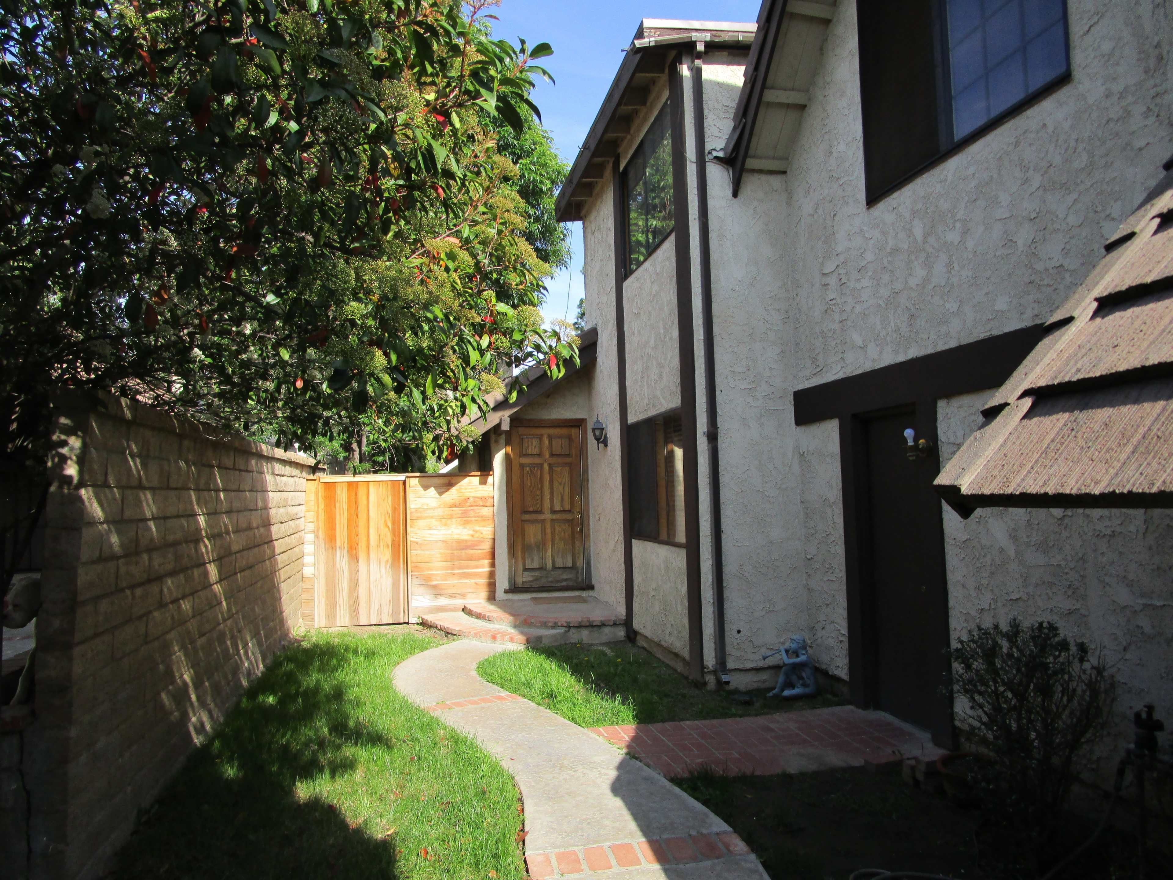 A winding stone pathway leads to a wooden front door, flanked by a grassy lawn and a fenced side yard.