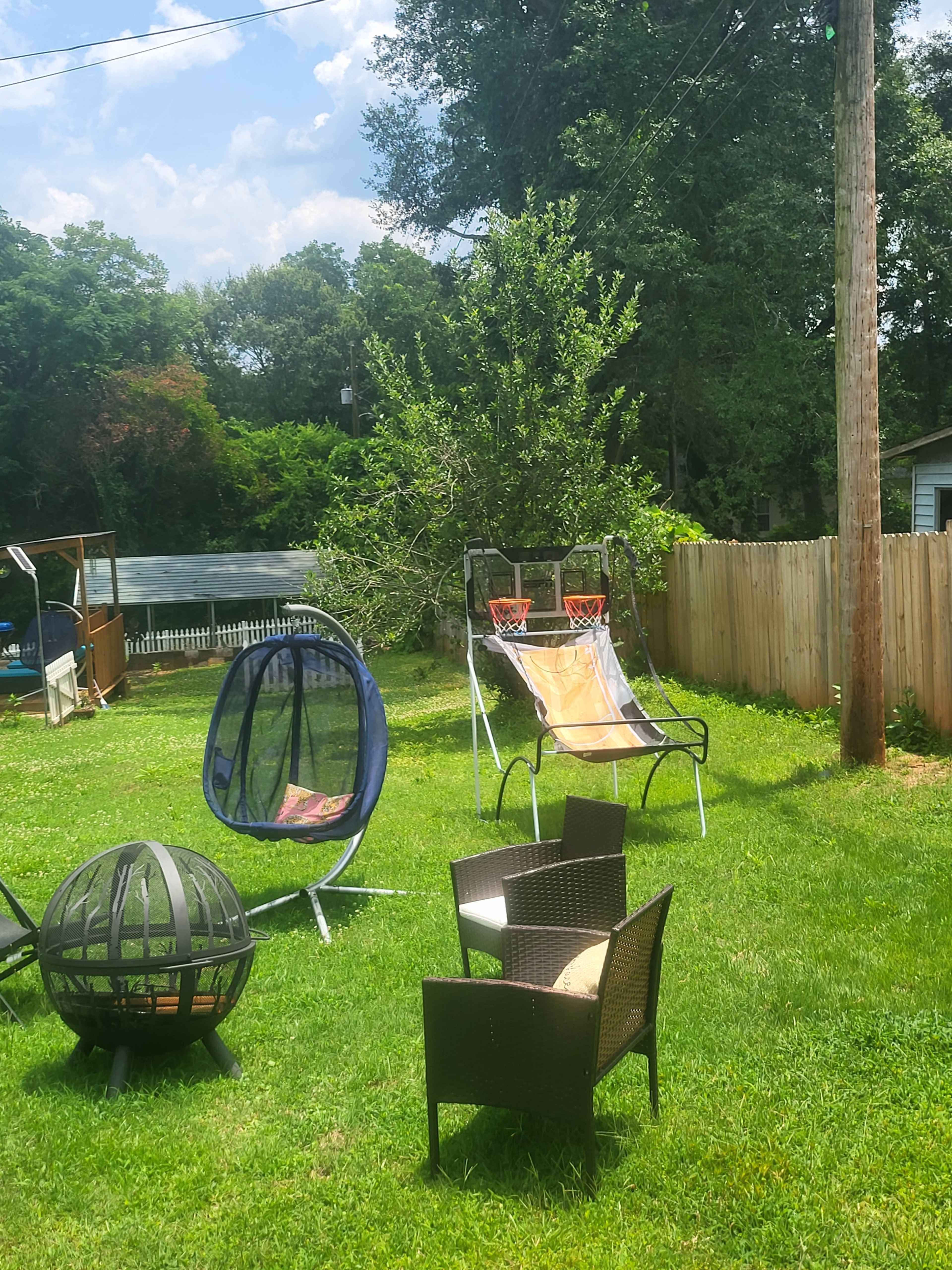 A backyard setting with various seating areas, including a fire pit, a hammock-style chair, and two basketball hoops.