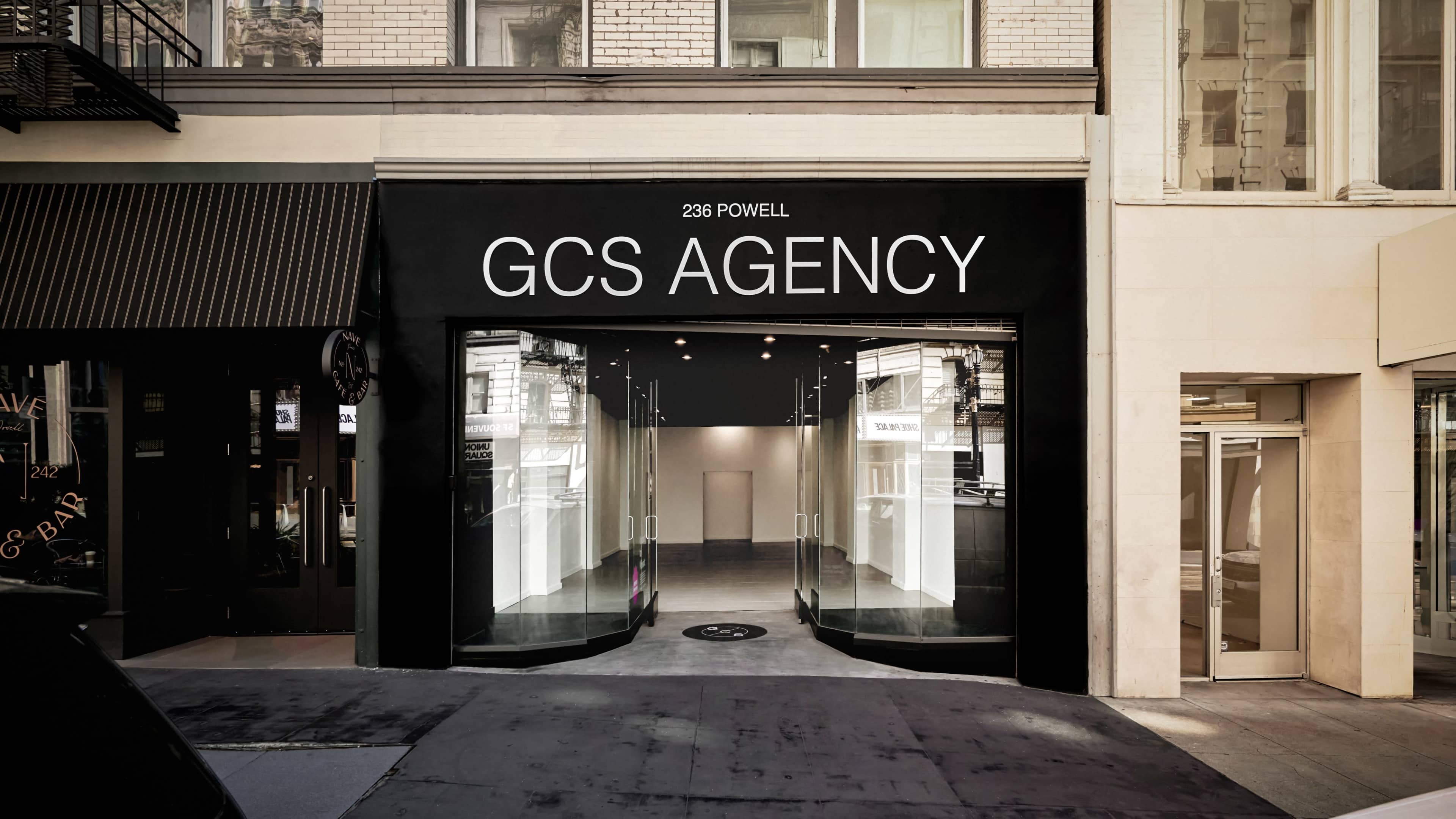 The image shows the exterior of a storefront labeled "GCS AGENCY" at 236 Powell Street, featuring large glass windows and a modern design.